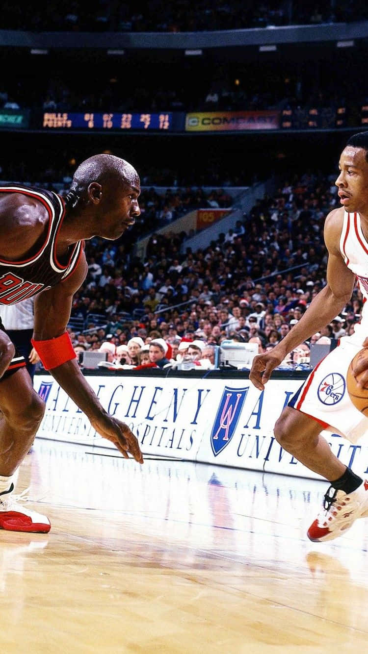 麥可喬丹在NBA比賽中，在歡呼的人群面前防守一名籃球運動員。 — Jordan Logo 壁紙