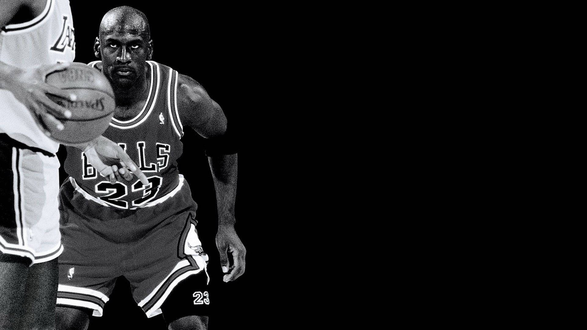麥可喬丹身穿公牛隊球衣，在籃球比賽中防守對手。 — Jordan Logo 壁紙
