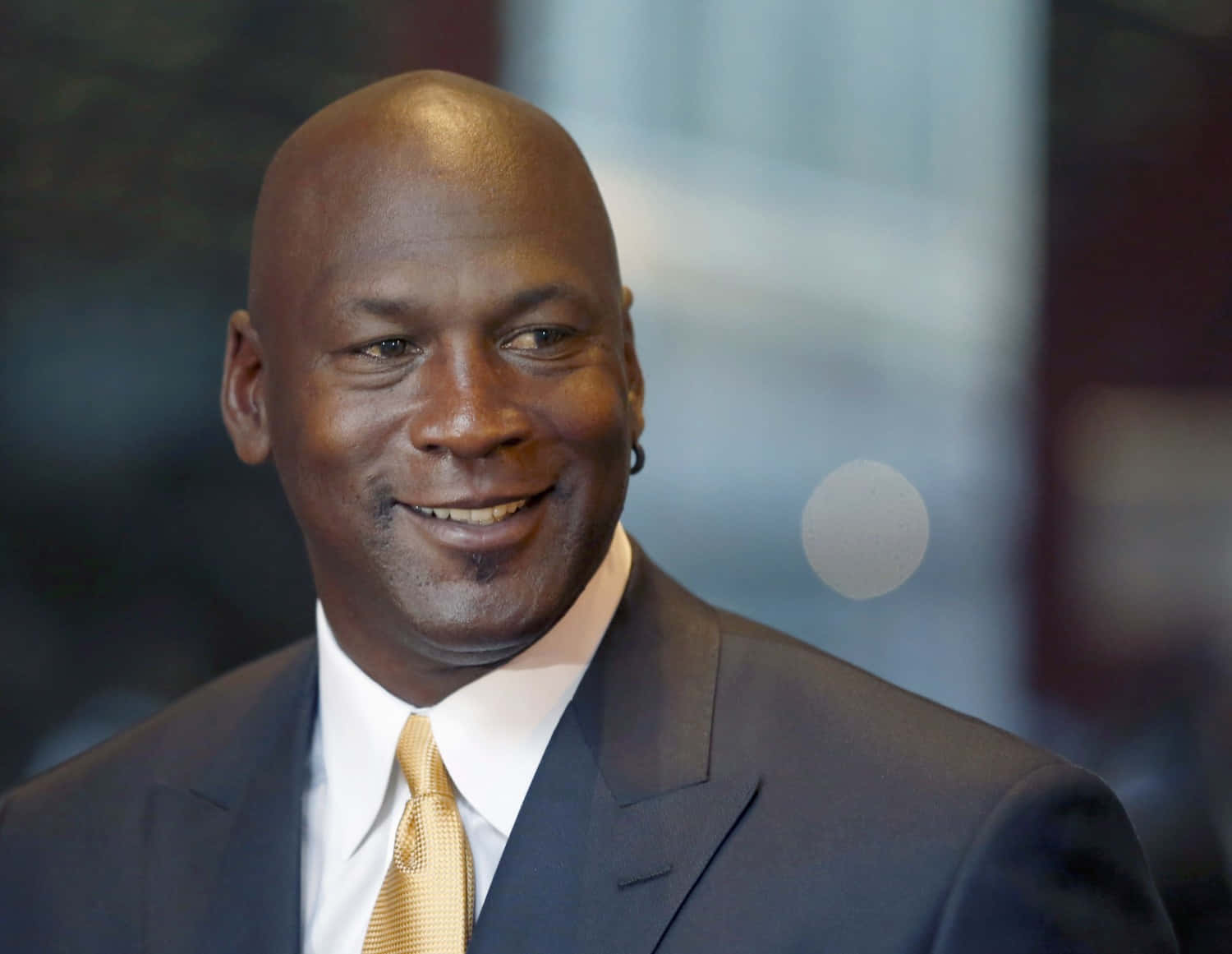 麥可喬丹身穿西裝和金色領帶對著鏡頭微笑。 — Jordan Logo 壁紙