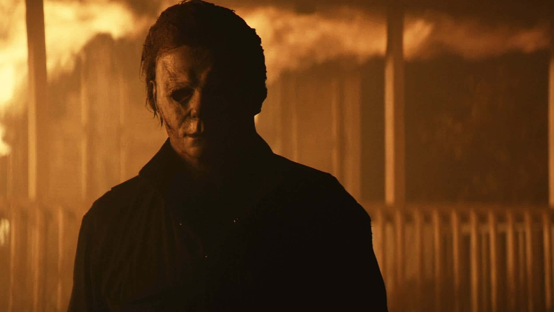  壁紙 — Michael Myers 以剪影形式站立，背景是火橙色，帶有煙霧和模糊的垂直結構。