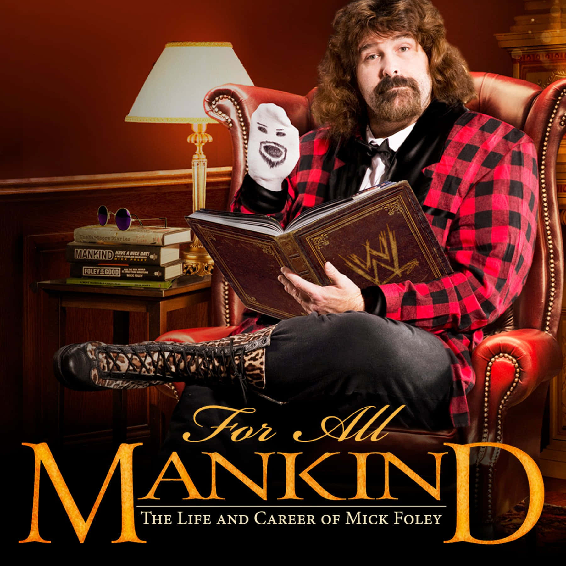 WWE 桌布 壁紙 — Mick Foley 坐在紅色皮椅上，手持一本 WWE 書籍和一個白色面具，身穿紅色格紋外套。
