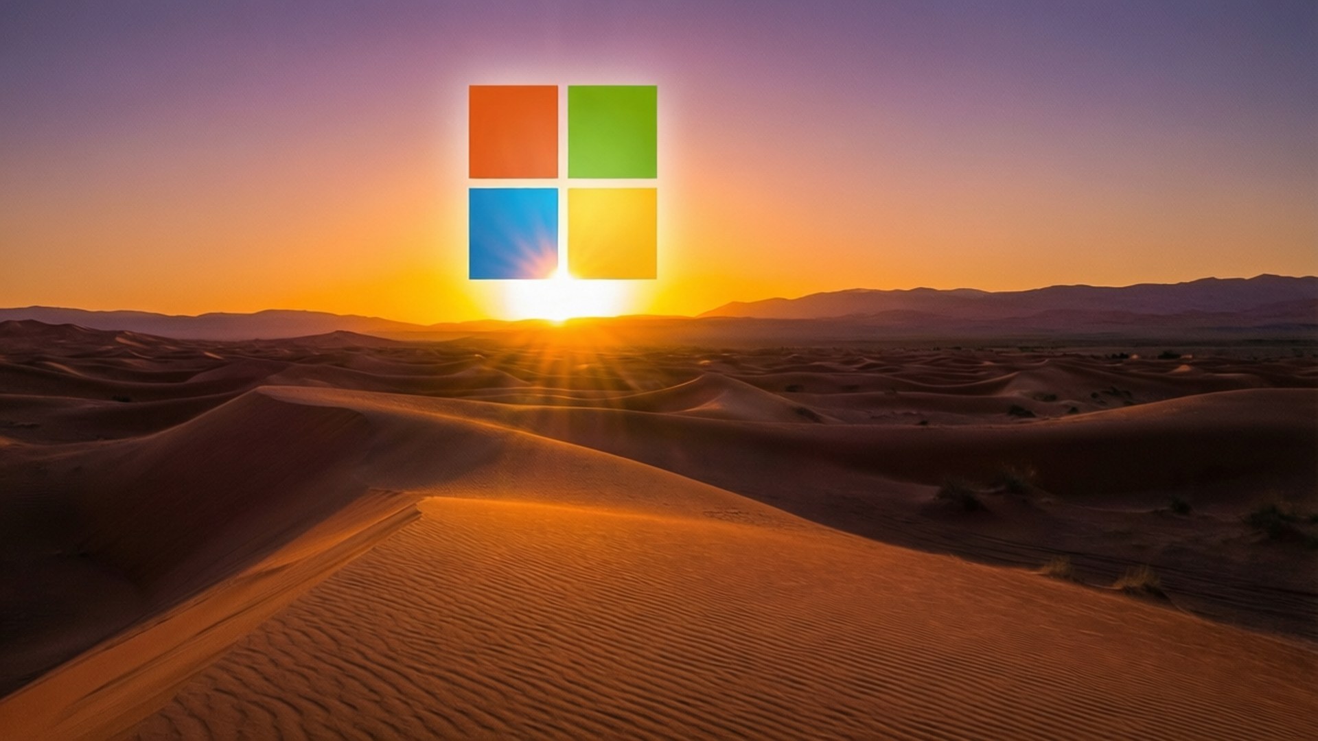 Desert Sunset Microsoft 壁紙 — Microsoft 標誌像日出般在暮色地平線上的金色沙漠沙丘上閃耀。