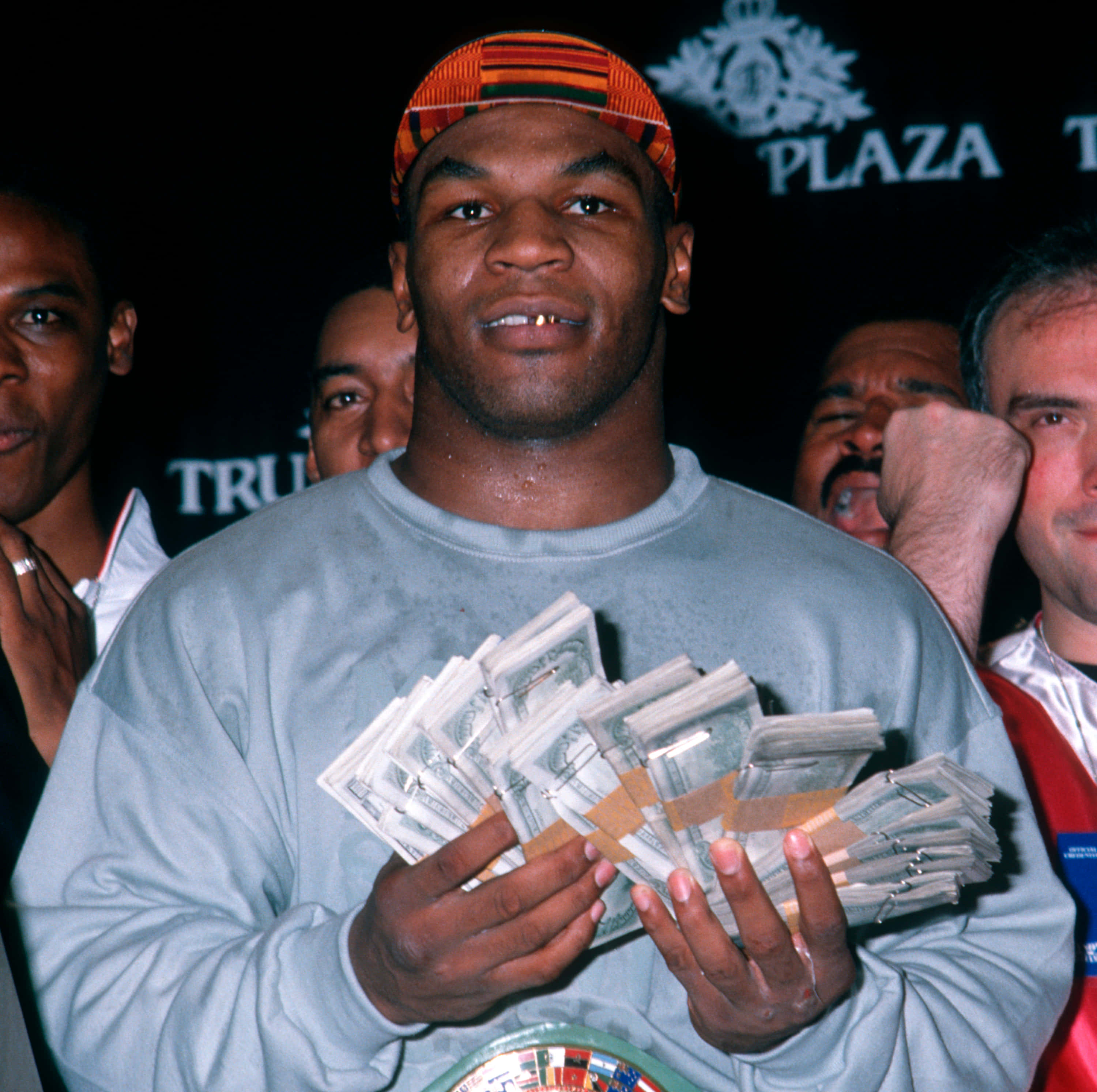 麥克·泰森 桌布 壁紙 — Mike Tyson 在 Plaza 活動中自豪地微笑，手持一疊疊現金，周圍有人。