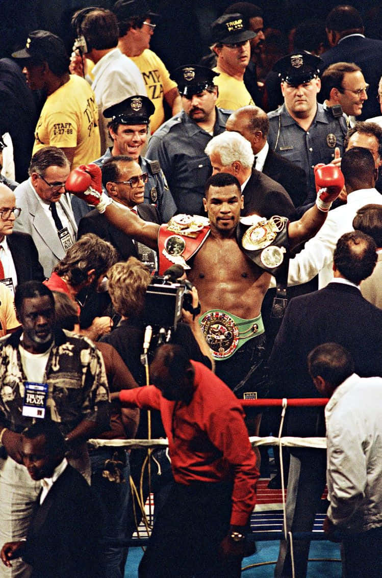 麥克·泰森 桌布 壁紙 — Mike Tyson 在擂台上高舉雙臂慶祝勝利，佩戴冠軍腰帶，被警察和媒體包圍。