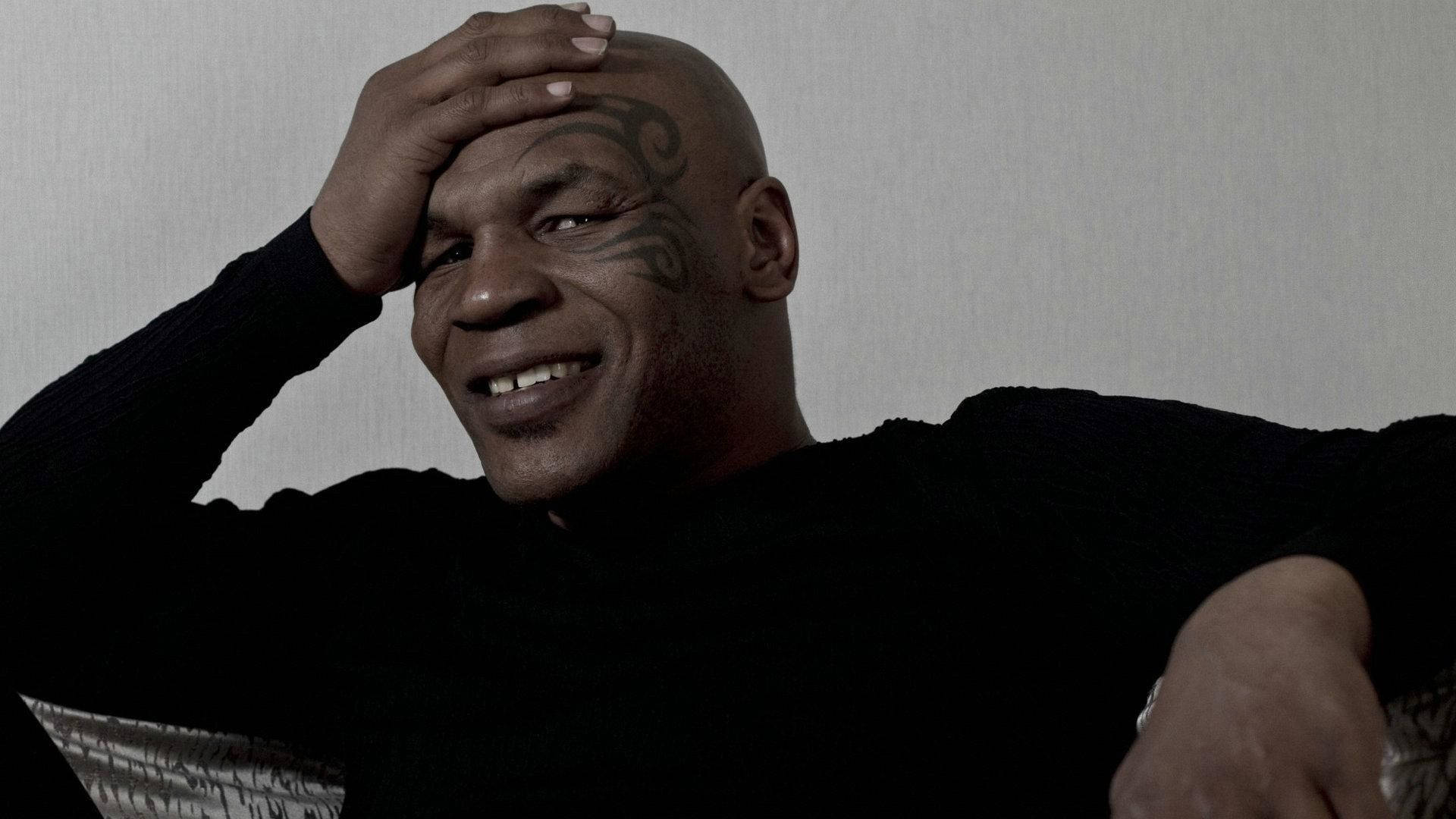 麥克·泰森 桌布 壁紙 — Mike Tyson 在昏暗燈光下對著素色牆壁，將手放在額頭上溫暖地微笑。