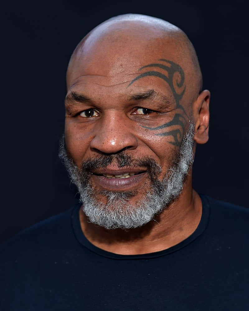 麥克·泰森 桌布 壁紙 — Mike Tyson 在深色背景下溫暖地微笑，他標誌性的部落紋身清晰可見於太陽穴。