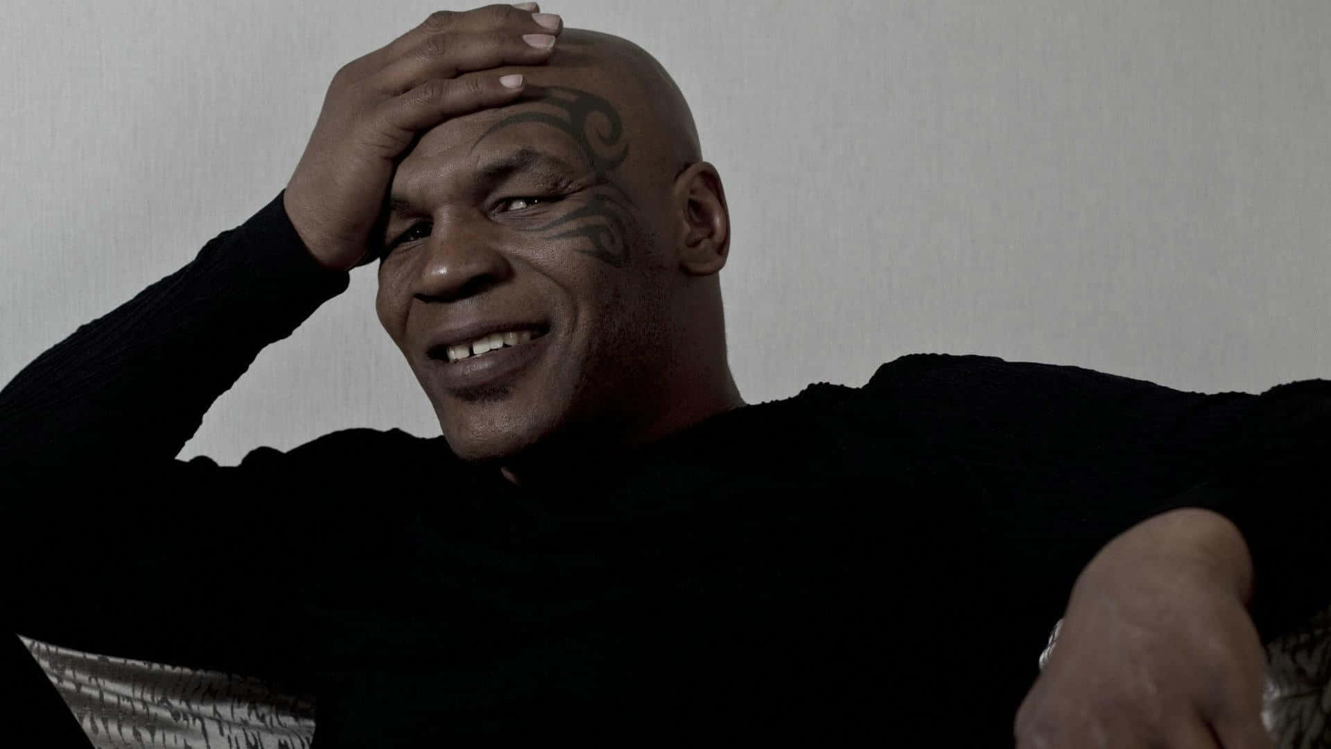 麥克·泰森 桌布 壁紙 — Mike Tyson 溫暖地微笑，將手放在頭上靠著素牆。