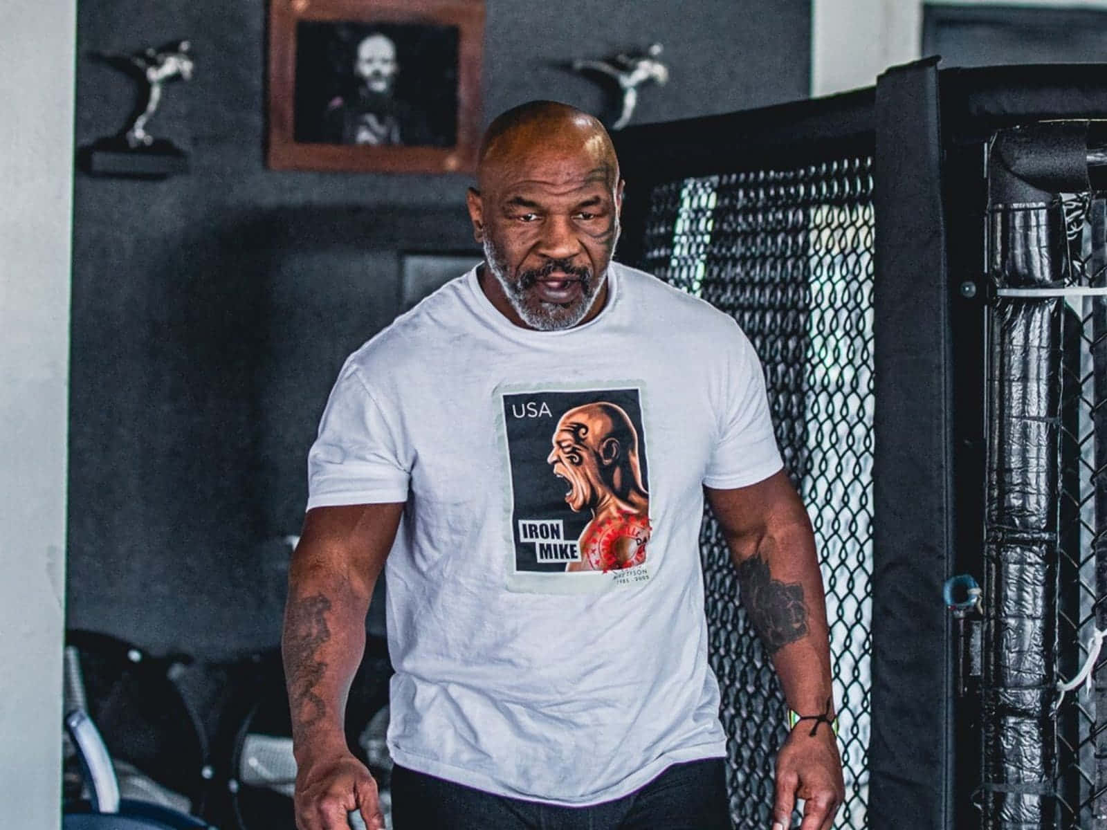 麥克·泰森 桌布 壁紙 — Mike Tyson 站在健身房，身穿印有「Iron Mike」圖案的白色T恤，手臂上的刺青清晰可見。