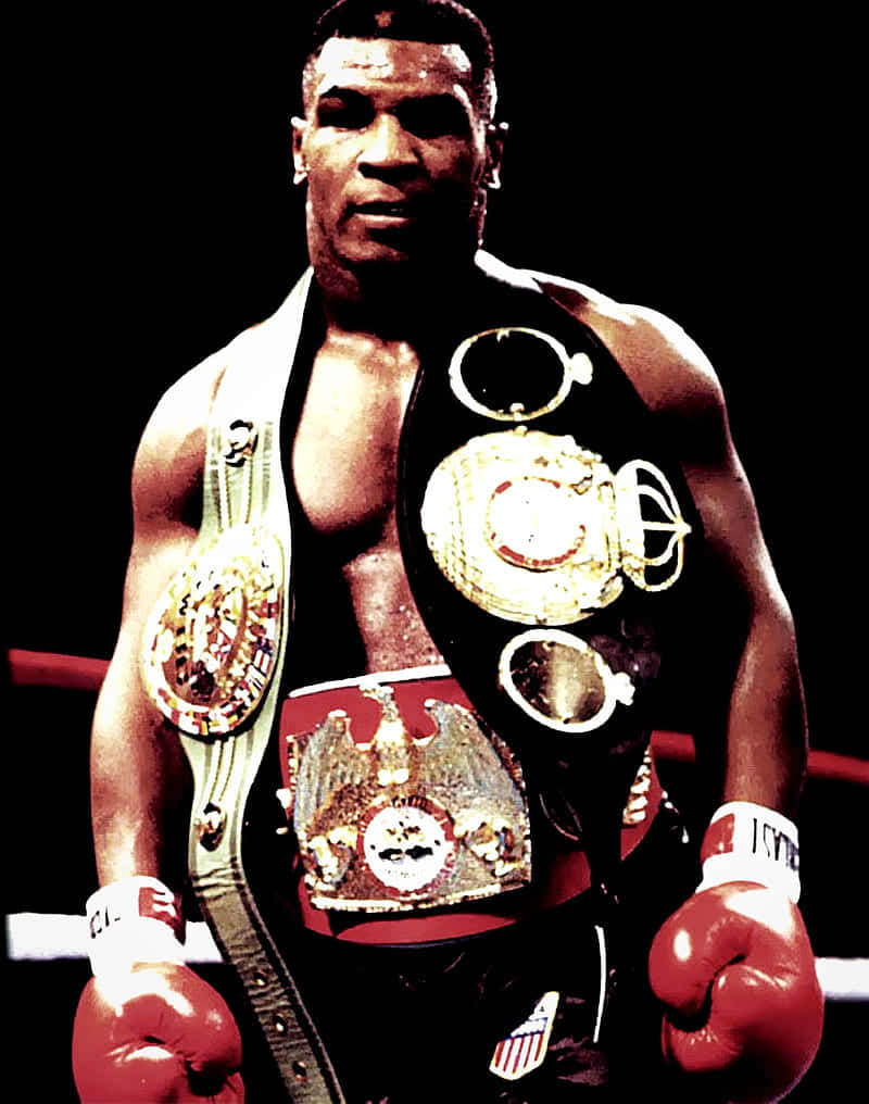 麥克·泰森 桌布 壁紙 — Mike Tyson 站在拳擊台上，佩戴多條冠軍腰帶和紅色手套，在戲劇性的聚光燈下。