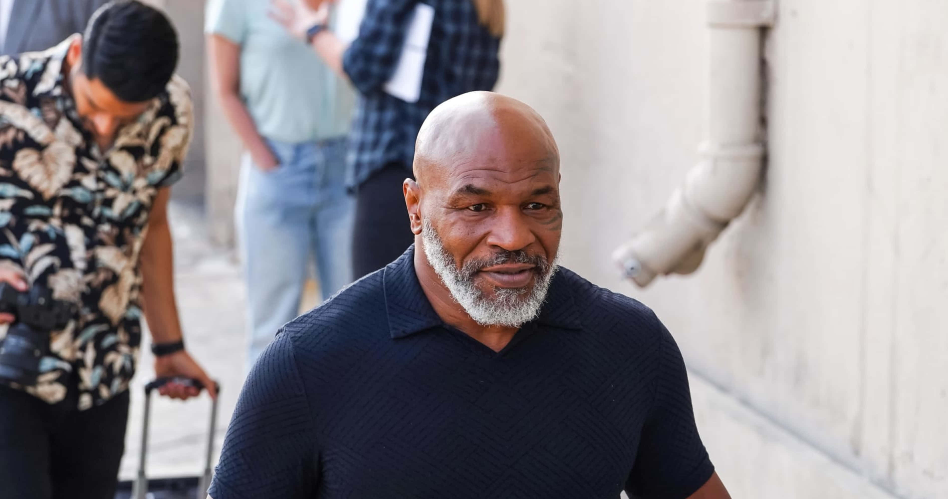 麥克·泰森 桌布 壁紙 — Mike Tyson 自信地走在陽光普照的城市小巷中，身後跟著一位攝影師。