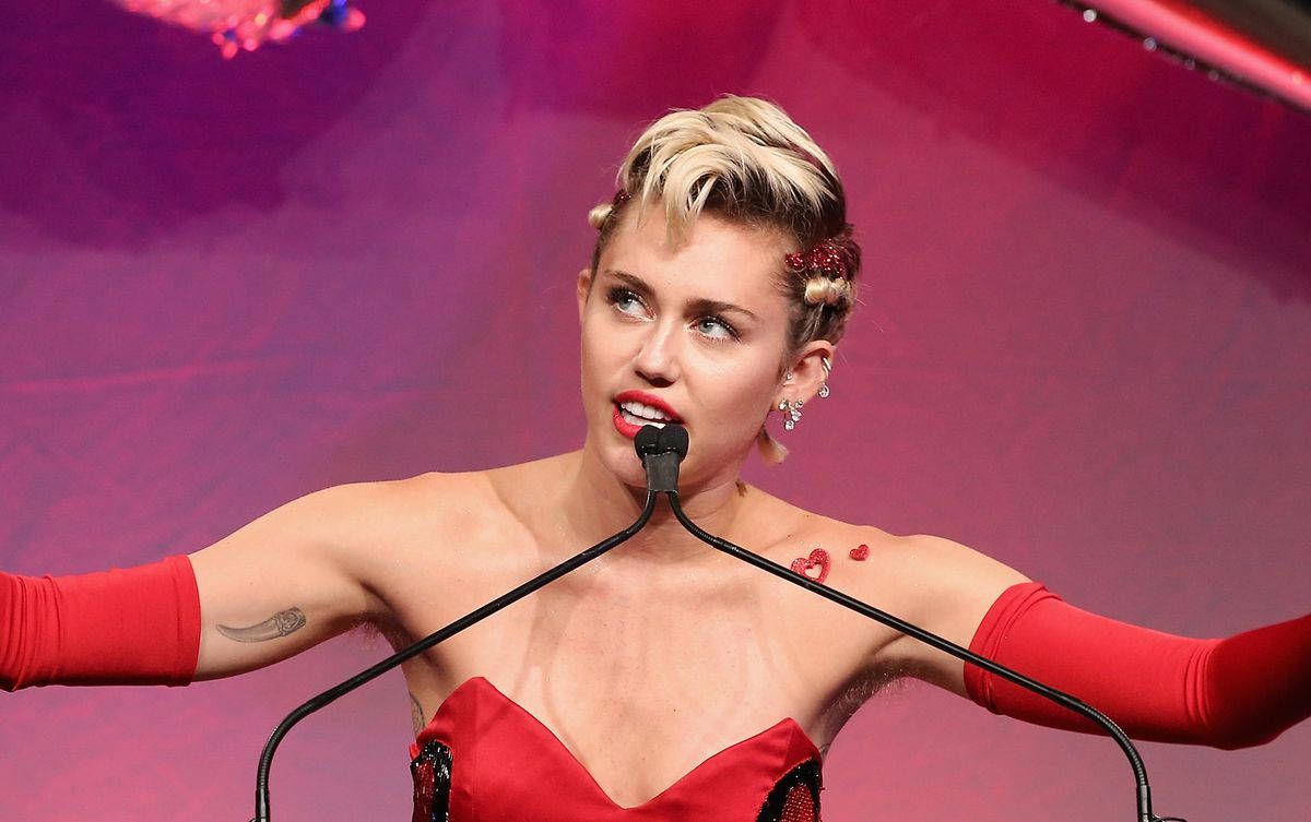 紅色動圖 桌布 壁紙 — Miley Cyrus 在舞台上穿著大膽的紅色服裝，雙臂伸展，背景是充滿活力的粉紅色。