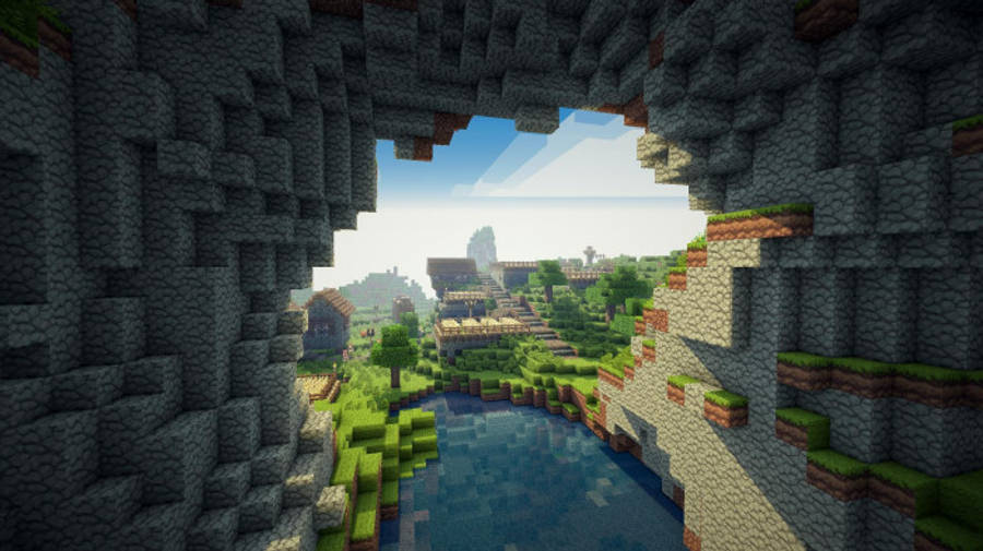 房屋 桌布 壁紙 — Minecraft洞穴入口展現出一個充滿活力的像素風景，其中有河流、樹木和遠處的村莊，在明亮的日光下。