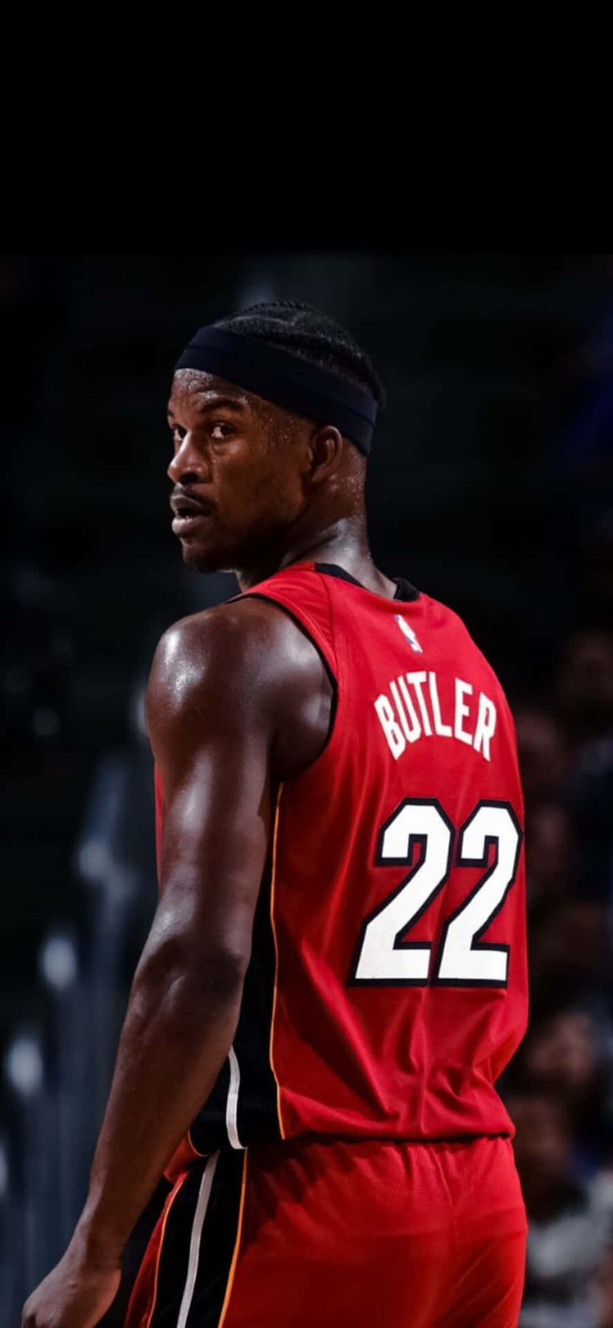  壁紙 — 一名身穿紅色邁阿密熱火球衣、背號22、背後印有BUTLER名字的籃球運動員，站在燈光昏暗的球場上。