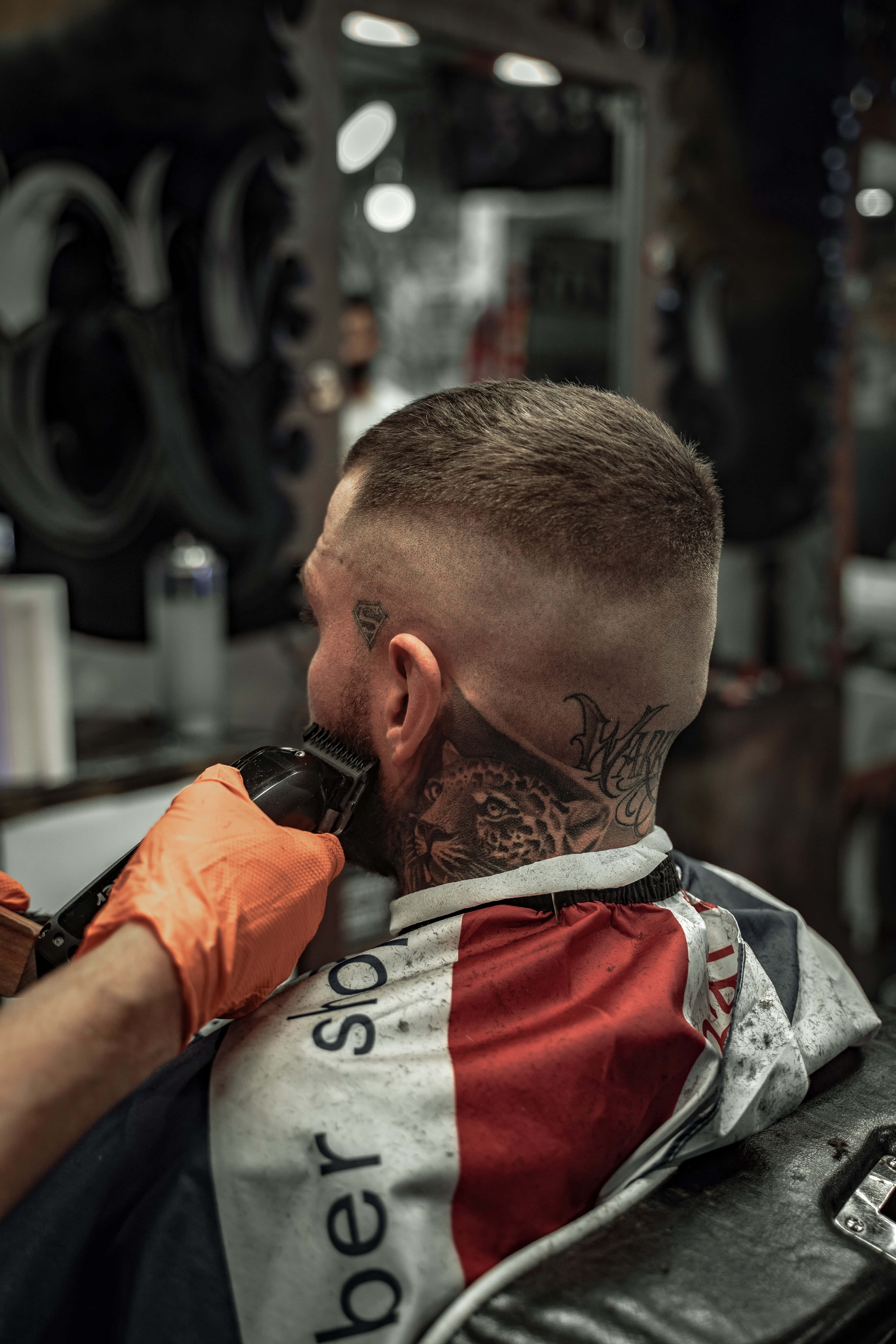 Barber 桌布 壁紙 — 一名頸上有豹紋刺青的男子，在理髮店穿著紅白斗篷理髮。