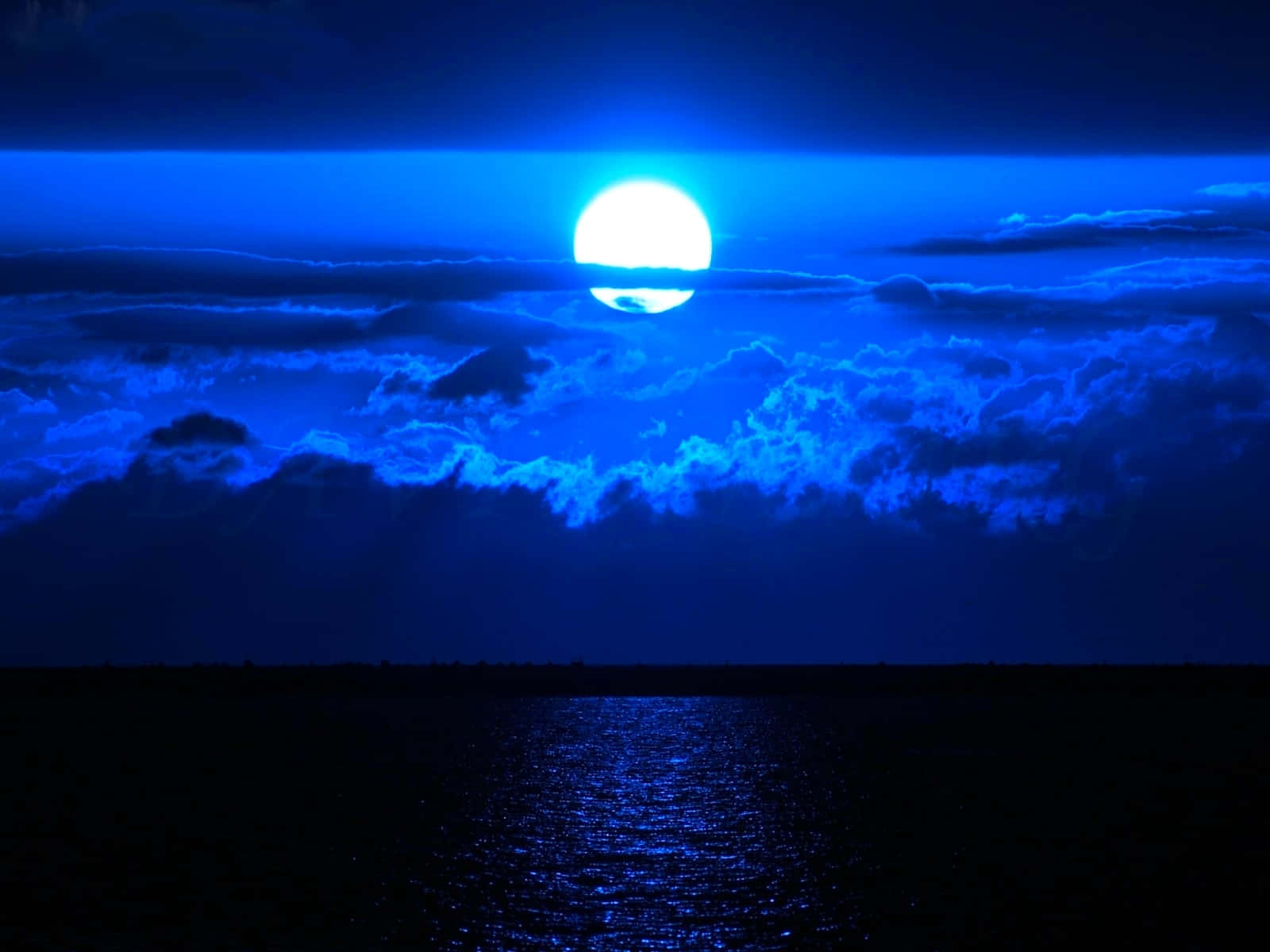  壁紙 — 一輪明亮的滿月在黑暗的海洋上方發光，將電光藍色投射在暴風雲和漣漪的水面上。