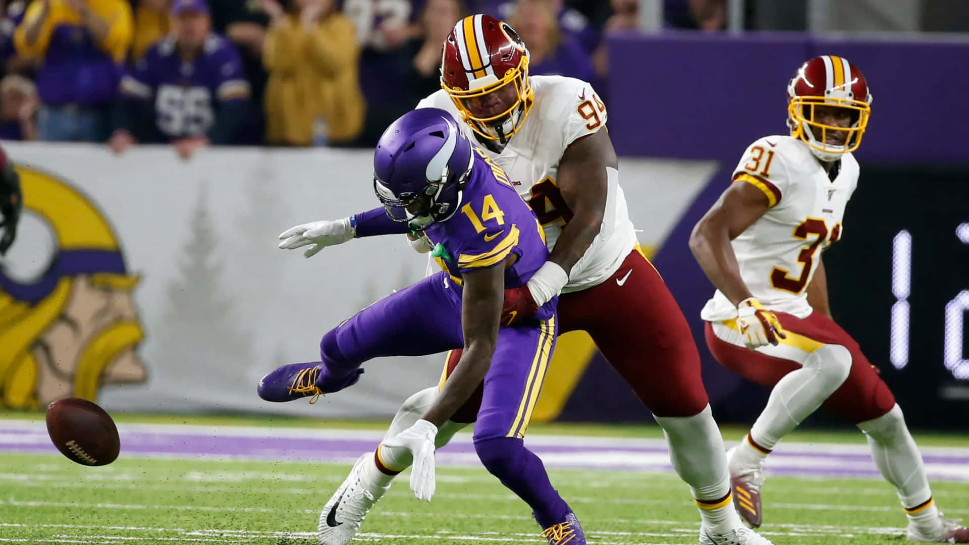  壁紙 — 在充滿活力的綠色球場上，一場激烈的NFL比賽中，一位身穿紫色的明尼蘇達維京人隊球員閃躲華盛頓美式足球隊的防守球員。