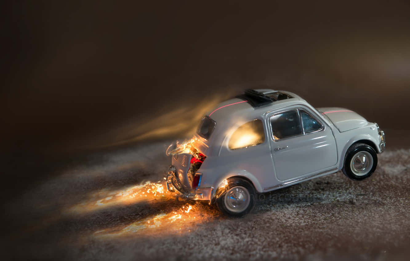 Fiat 500 桌布 壁紙 — 一輛微型銀色汽車在戲劇性燈光下撞上粗糙表面，爆發出火焰和火花。