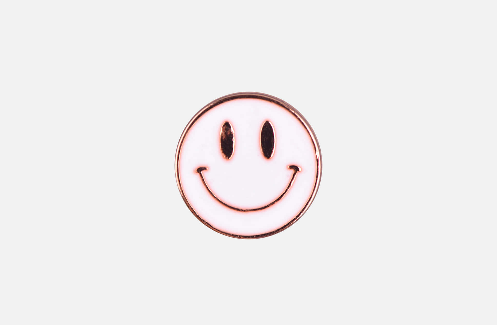  壁紙 — 一個極簡主義的琺瑯別針，帶有經典笑臉，黑色眼睛和彎曲的嘴巴，白色背景。