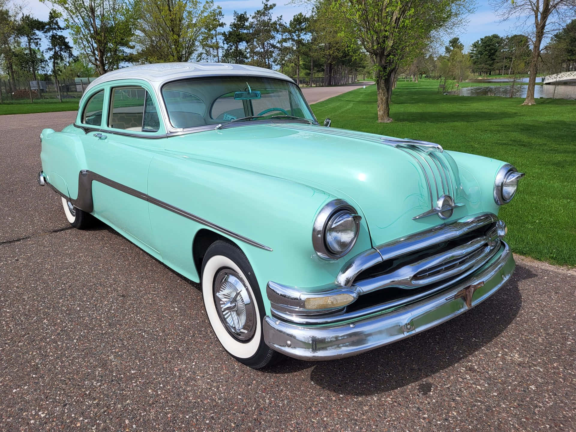 Pontiac Chieftain 桌布 壁紙 — 一輛薄荷綠色的經典汽車，帶有鍍鉻裝飾，在明亮的陽光下閃閃發光，停在鋪砌的車道上，旁邊是一個草地公園。