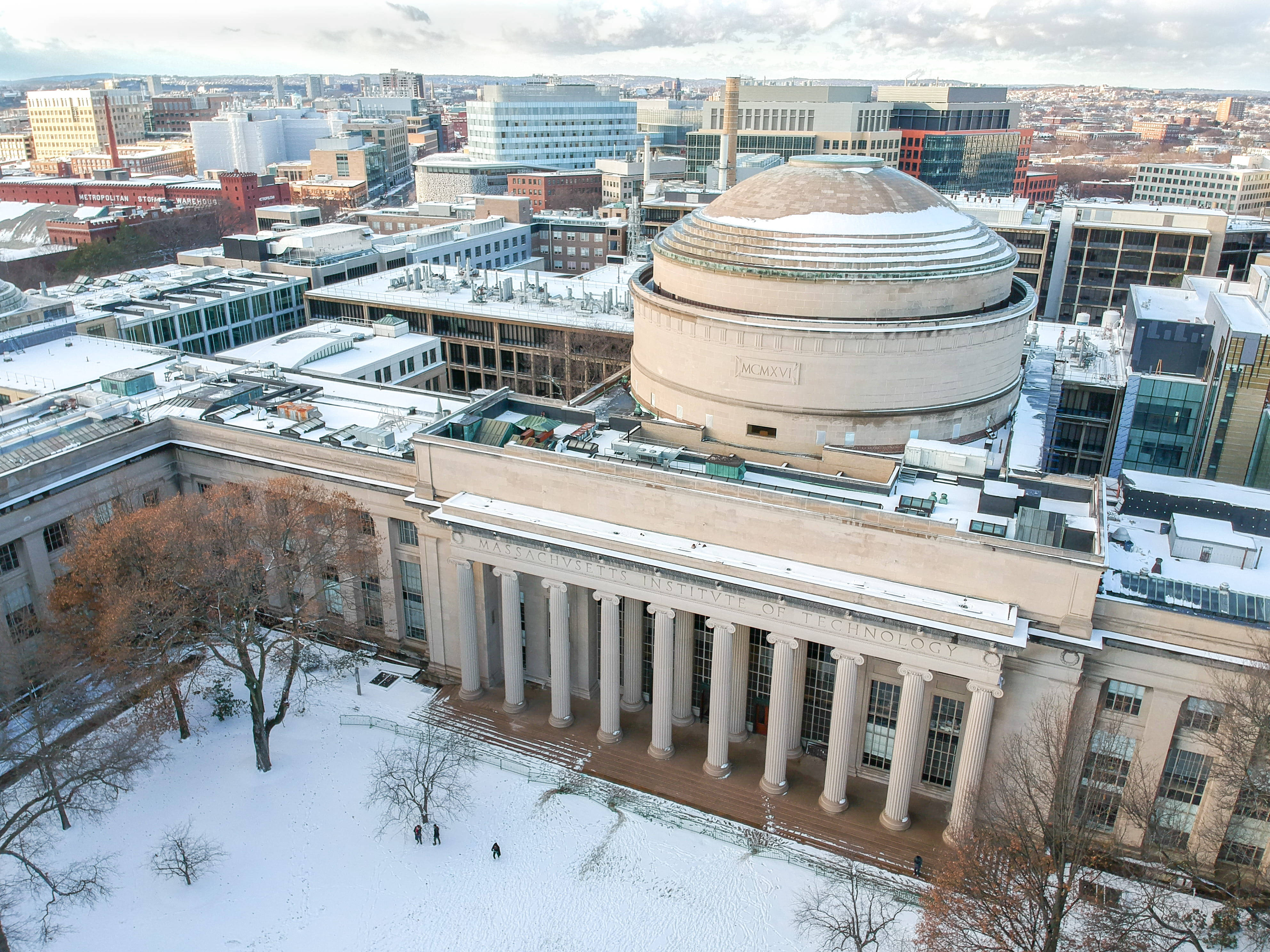學校 桌布 壁紙 — MIT標誌性圓頂建築的鳥瞰圖，被白雪覆蓋，冬日裡有光禿的樹木和城市景觀。