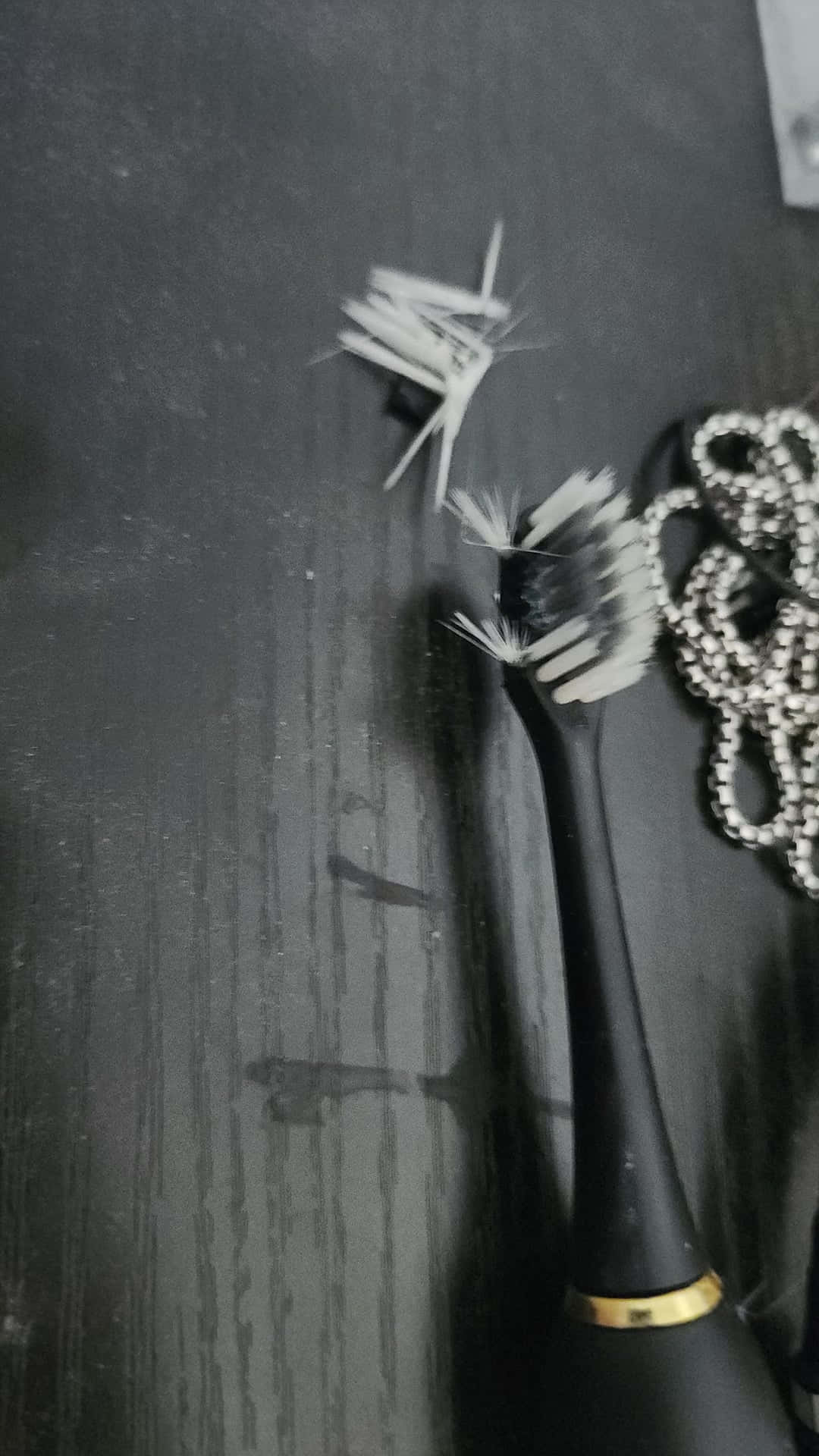  壁紙 — 一支磨損的電動牙刷，刷毛磨損，放在深色紋理表面上，旁邊有一條珠鏈。