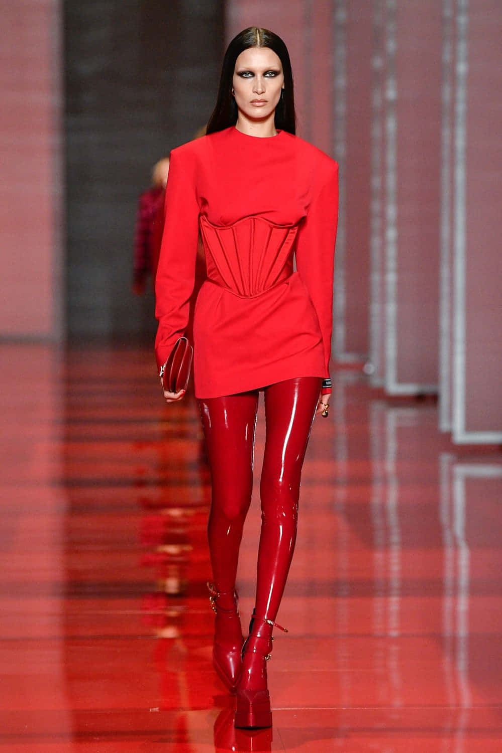 Red Clothing 桌布 壁紙 — 一位模特兒自信地走在光亮的紅色伸展台上，身穿大膽的紅色束腰連衣裙和相配的閃亮緊身褲。
