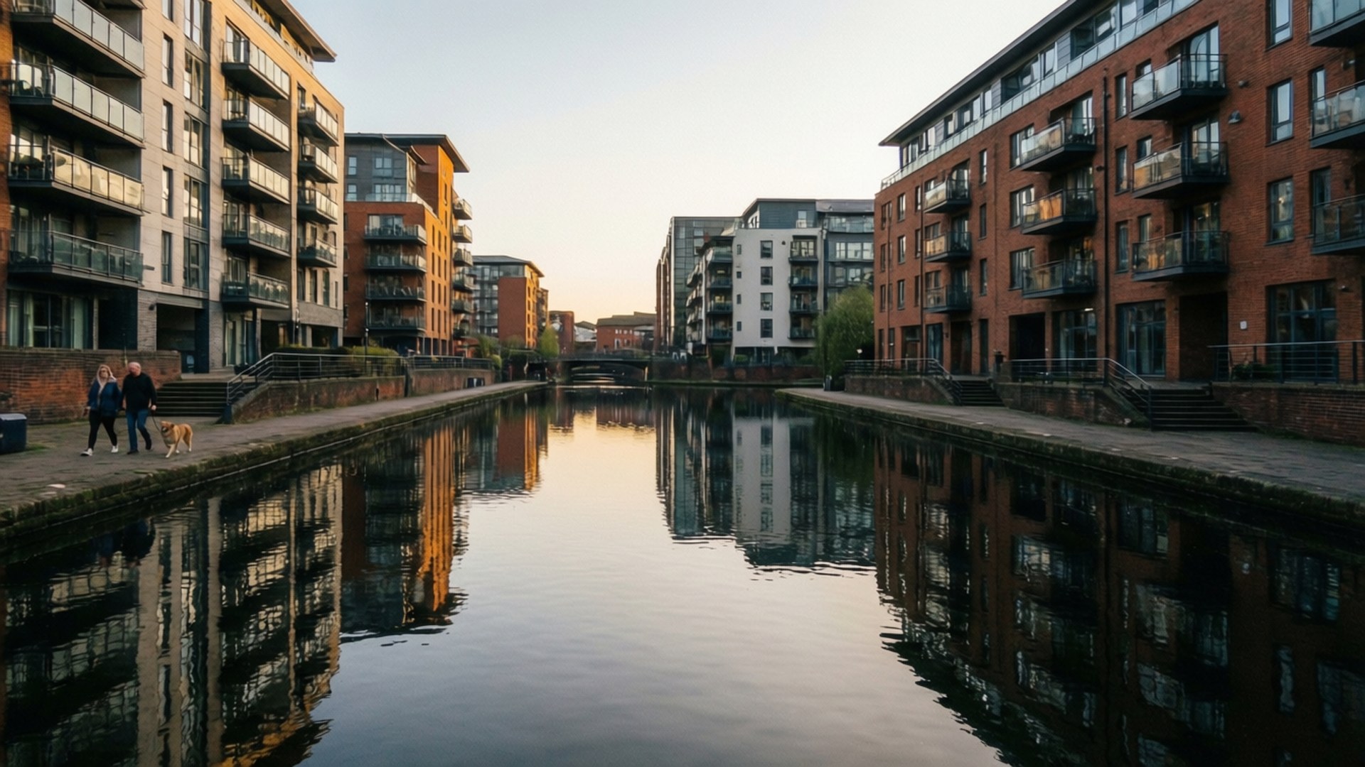 Brindleyplace Reflections 壁紙 — 現代磚砌公寓大樓沿著平靜的運河排列，反射著溫暖的日落色調，兩個人正沿著小徑遛狗。