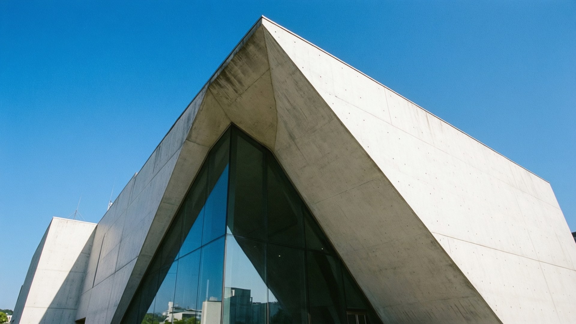 Museum Geometry 壁紙 — 一座現代混凝土建築，具有銳利的幾何角度和大型玻璃窗，在清澈的藍天下。