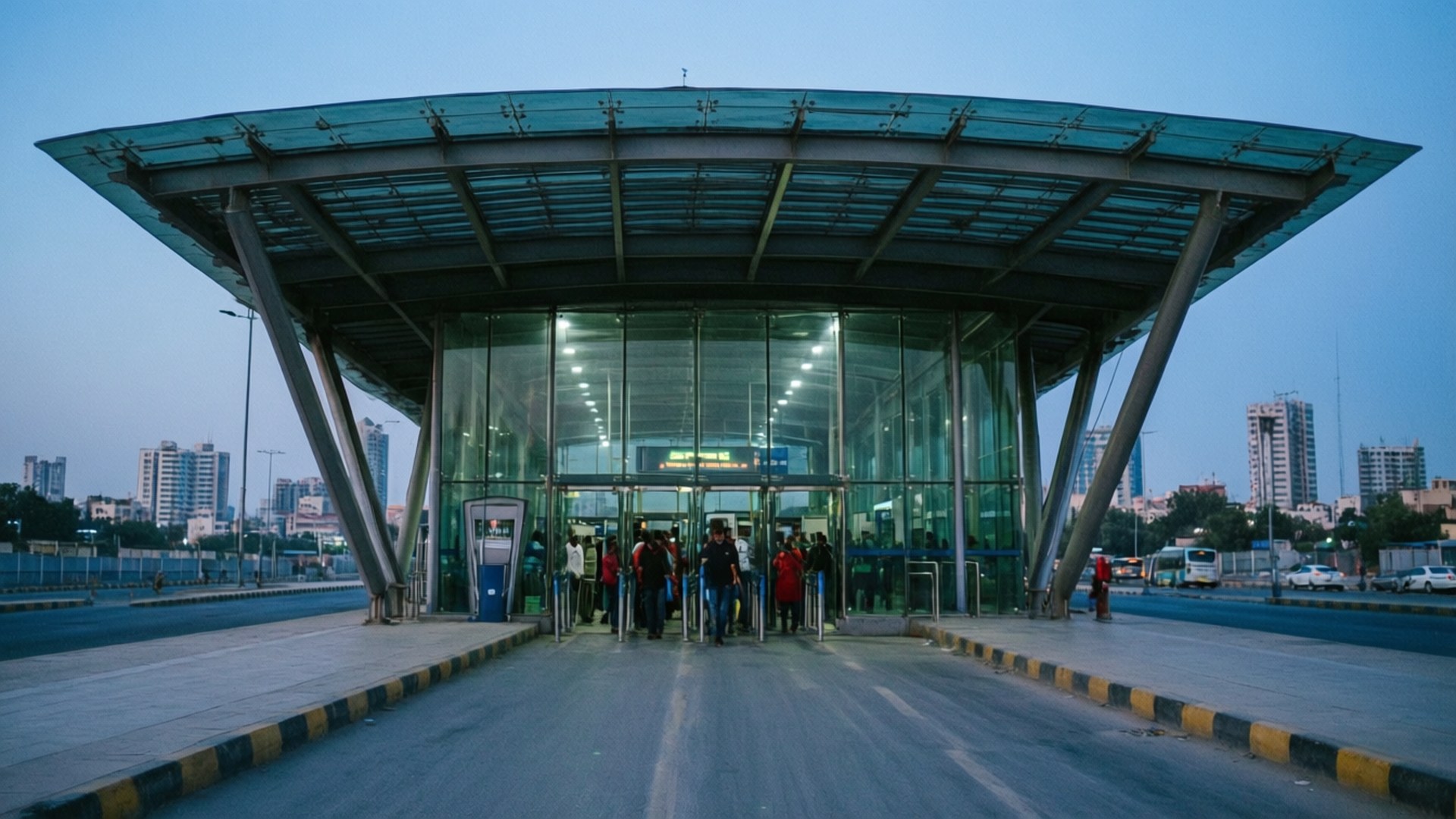 Lahore Metro Modern 壁紙 — 現代玻璃和鋼結構交通站入口，人們在黃昏時分進入，背景是城市天際線。