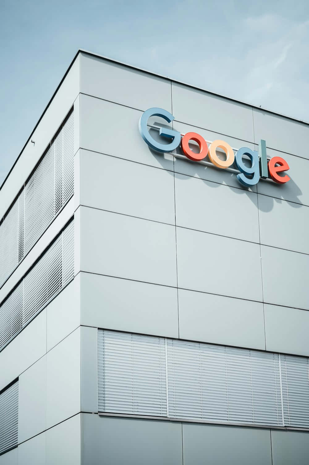 壁紙 — 現代白色建築角落，在清澈藍天下展示色彩繽紛的Google標誌。