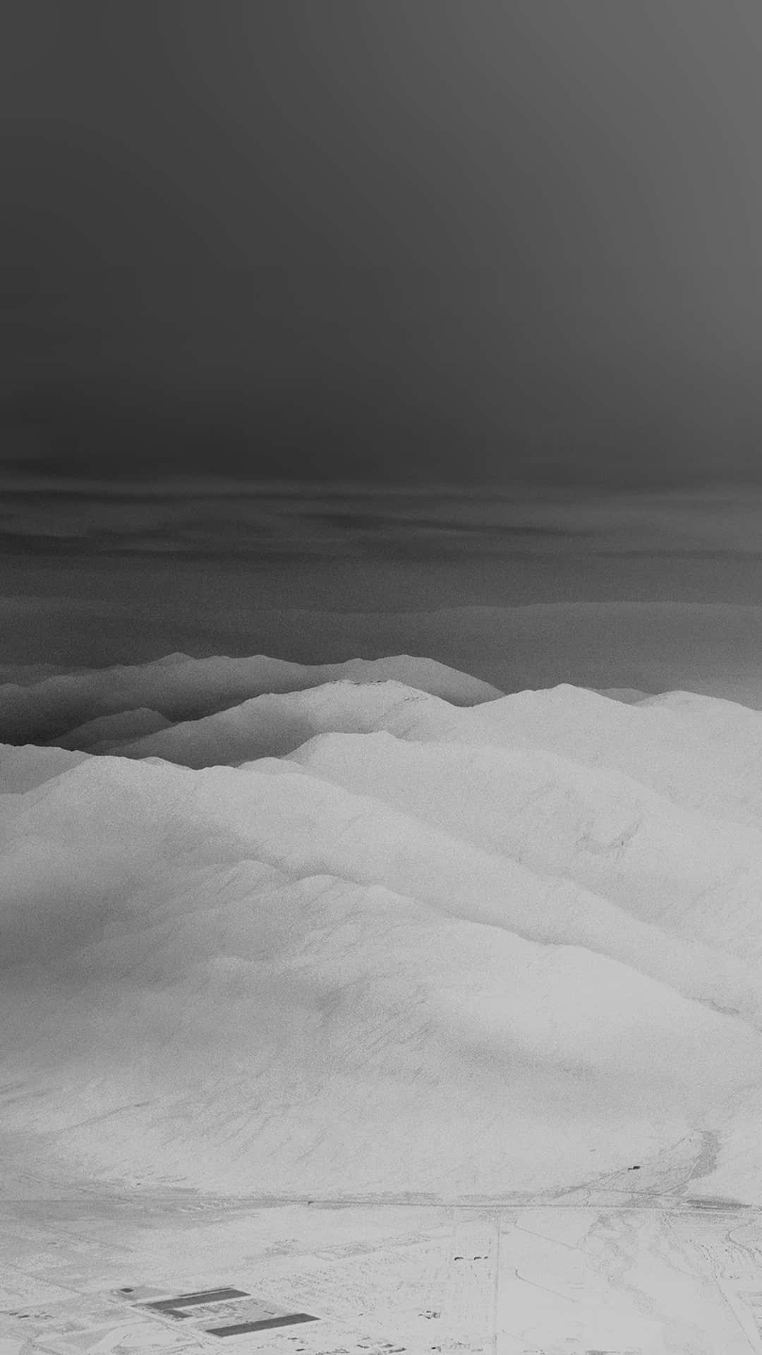  壁紙 — 白雪覆蓋的山脊單色航拍圖，背景為漸變灰色天空，帶有柔和陰影。