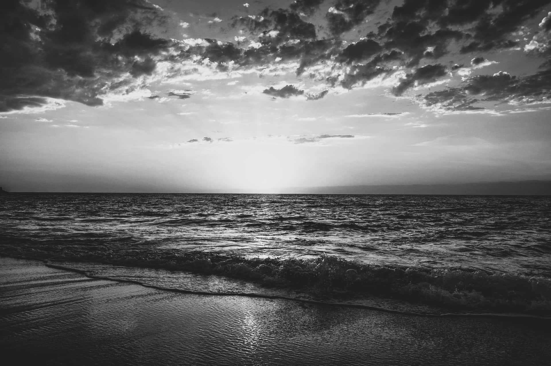  壁紙 — 在戲劇性的多雲天空下，紋理波浪滾滾湧向海岸的單色海灘日落場景。