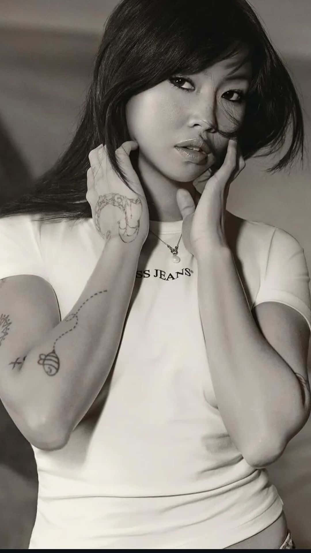  壁紙 — 一位手臂和手上有刺青的女性黑白肖像，身穿白色T恤，以沉思的表情直視鏡頭。