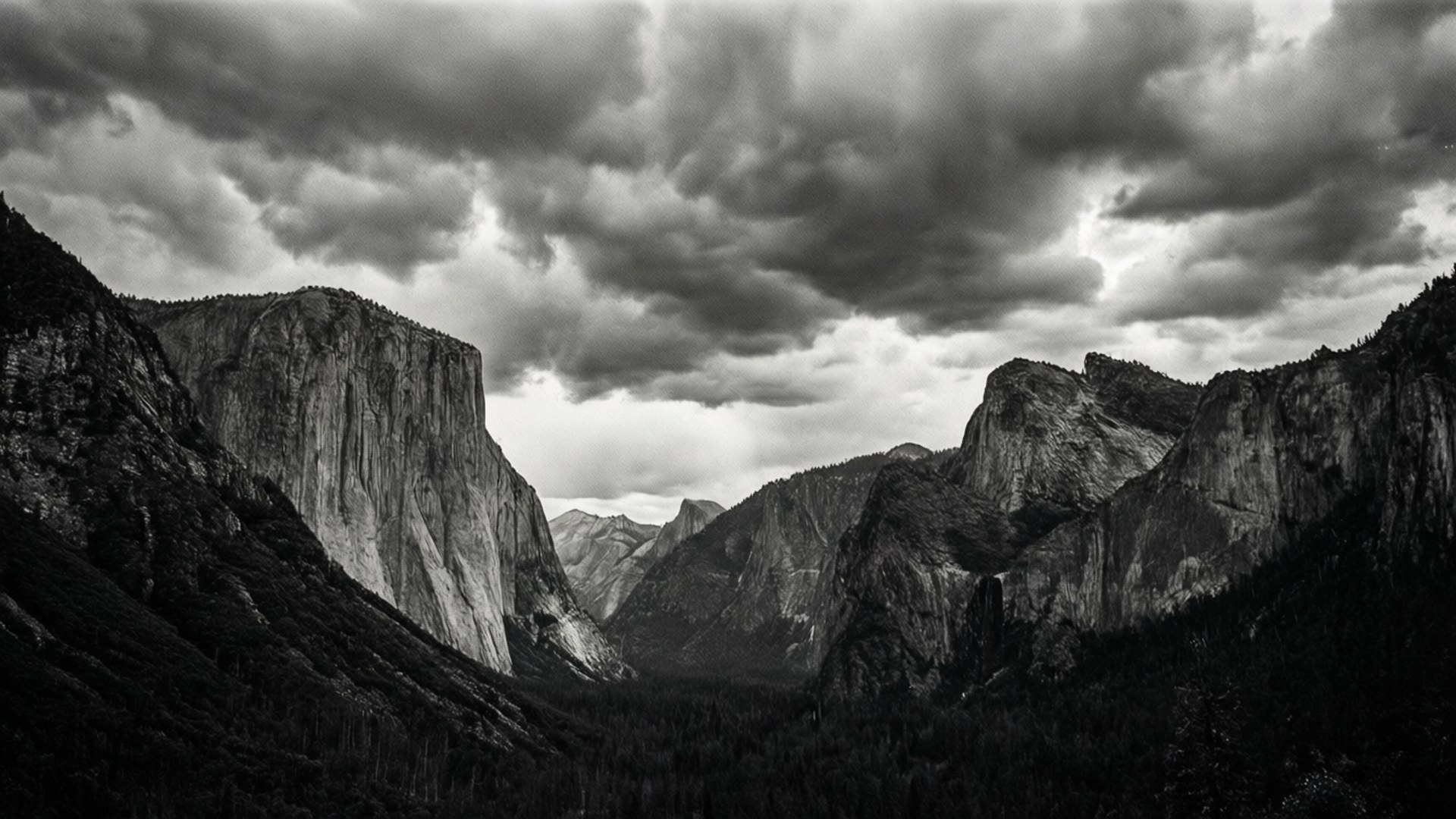 Monochrome El Capitan 壁紙 — 在戲劇性的多雲天空下，宏偉的花崗岩懸崖框住了優勝美地山谷的黑白景觀。