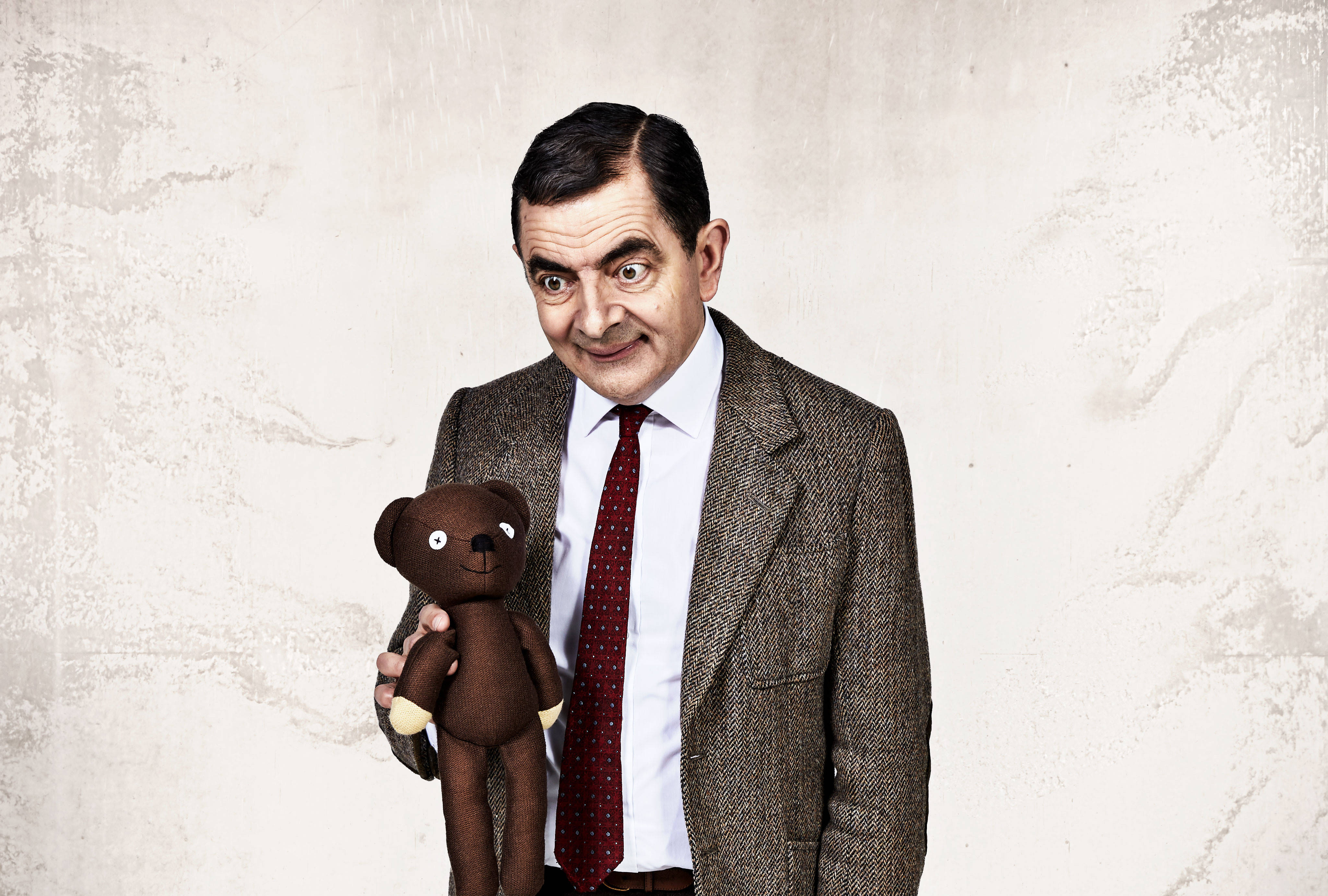 Mr Bean 穿著粗花呢西裝，拿著一隻棕色泰迪熊，露出頑皮的笑容。 — 4K 壁紙