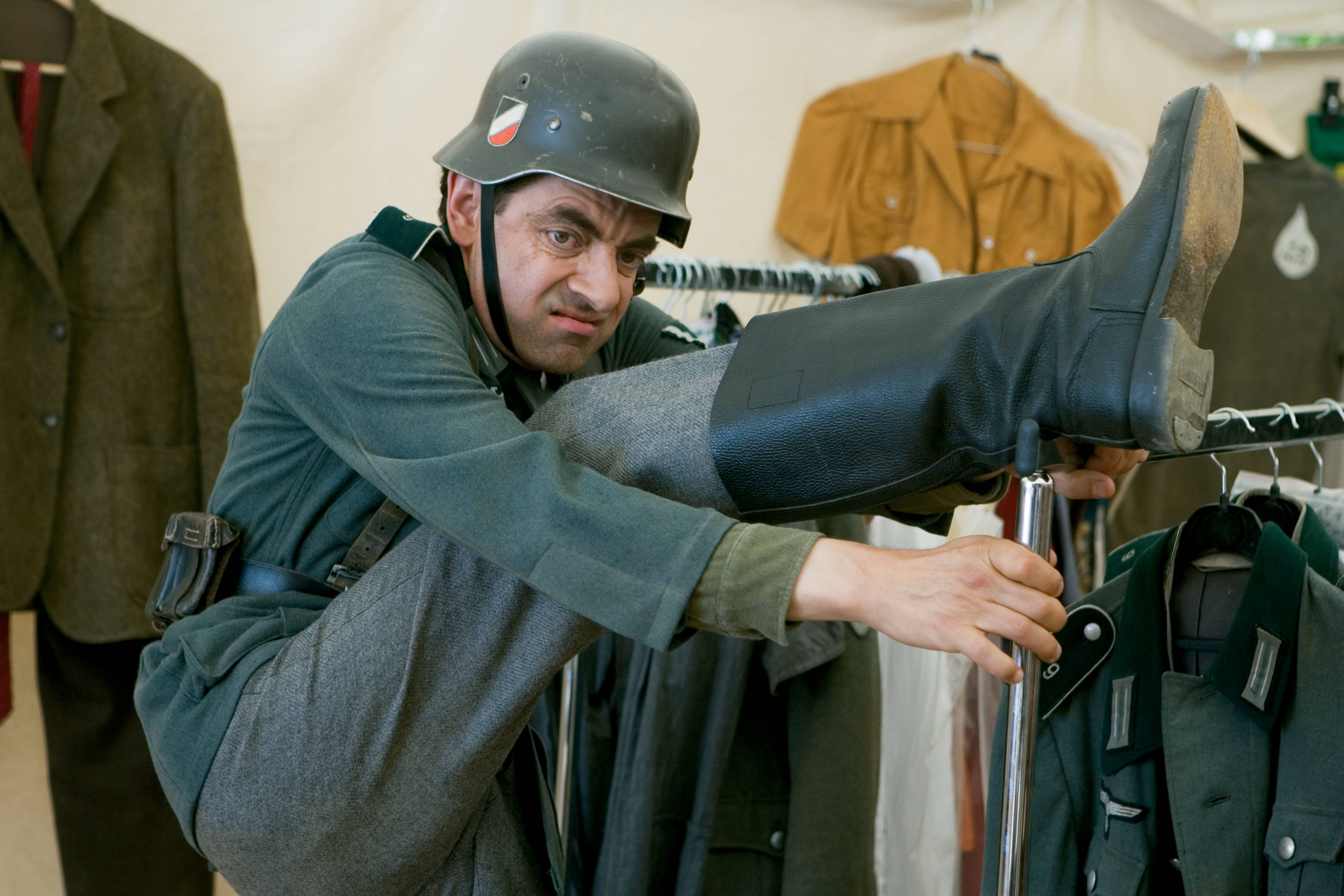 Mr Bean 穿著二戰軍服，在衣架上平衡身體，試穿靴子。 — 4K 壁紙