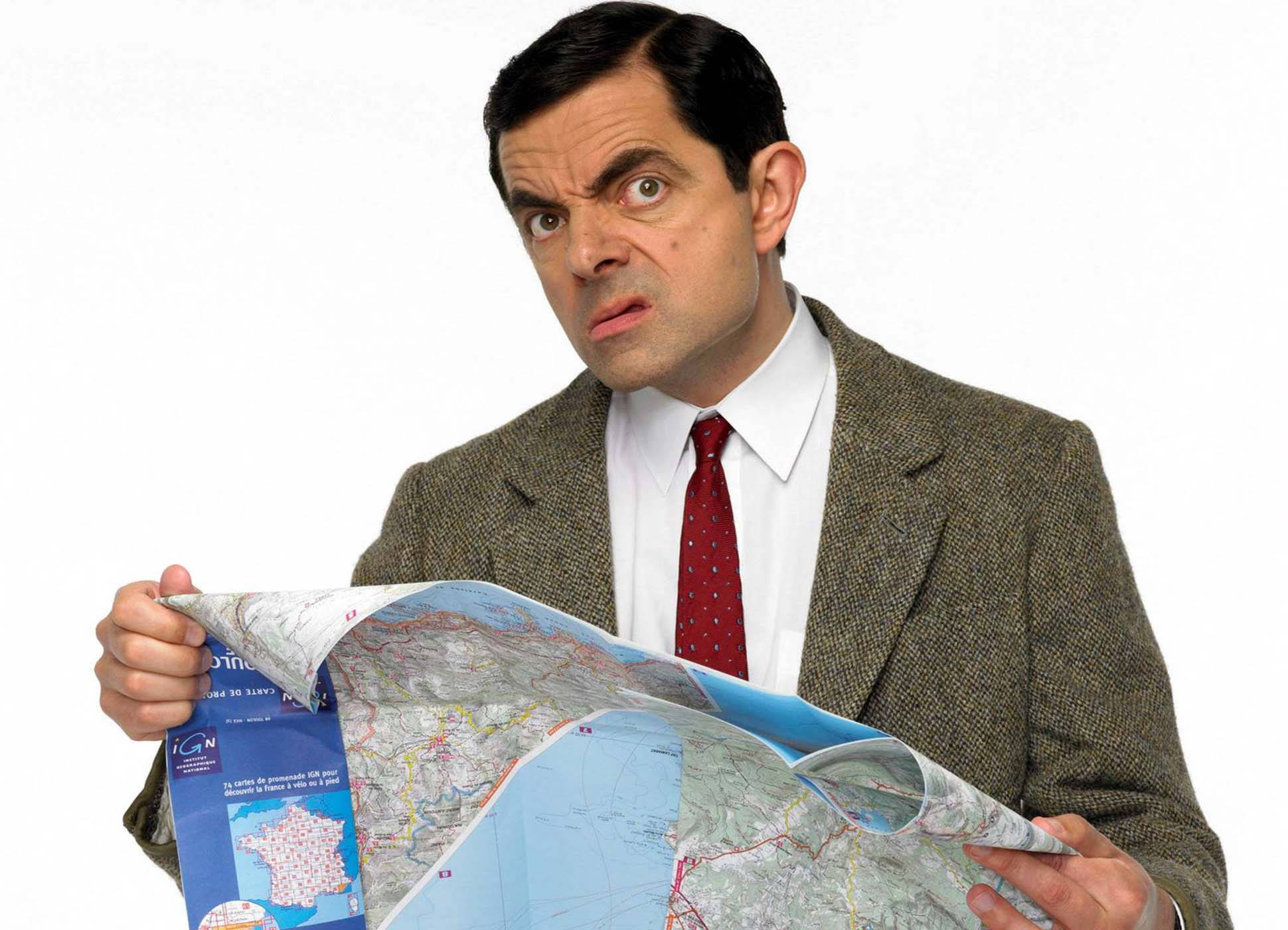豆豆先生 桌布 壁紙 — Mr. Bean 困惑地盯著一張皺巴巴的地圖，表情滑稽地困惑，背景是純白色。