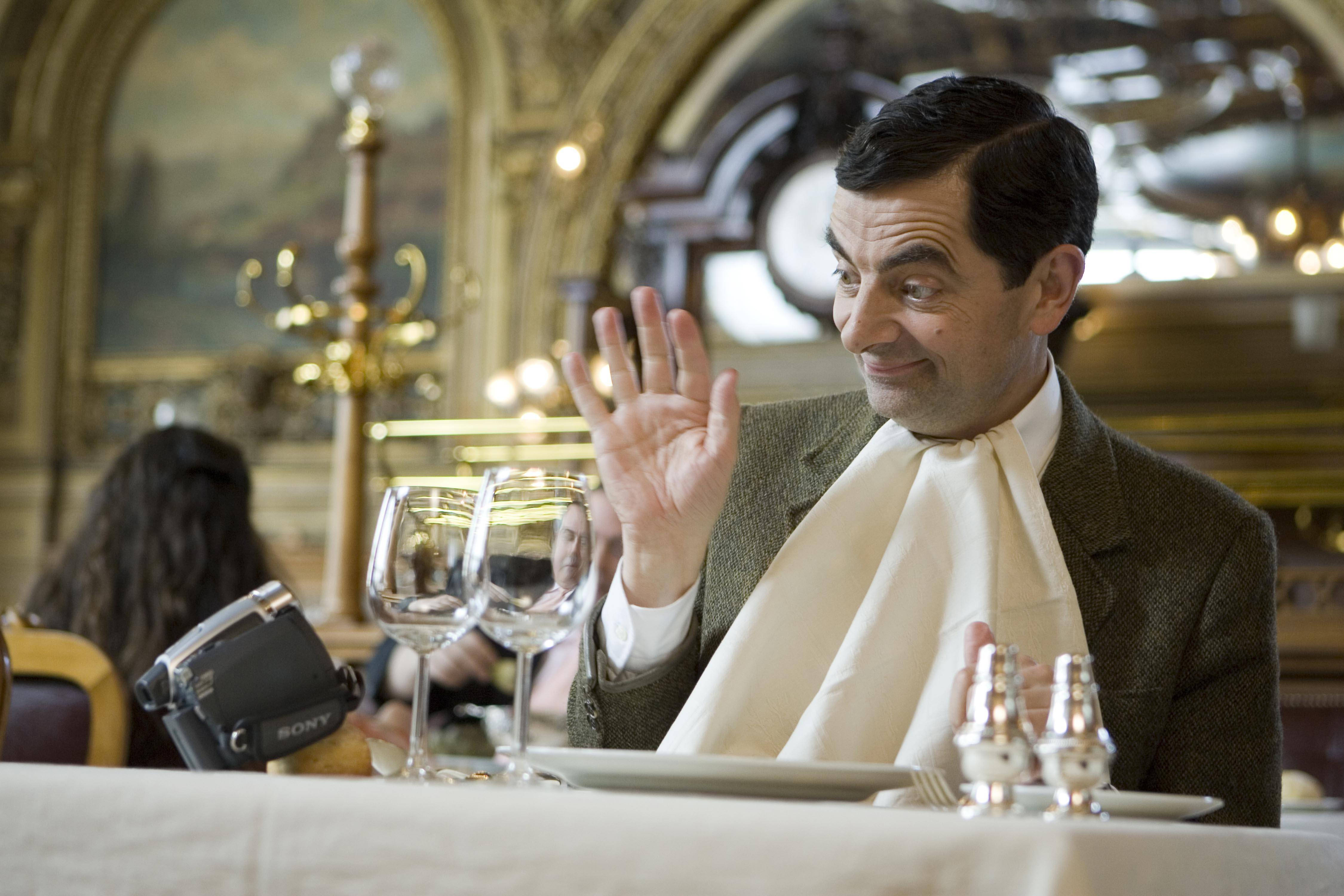 4K 桌布 壁紙 — Mr Bean 在一個華麗的金色裝飾和酒杯的高級餐廳桌上開心地揮手。