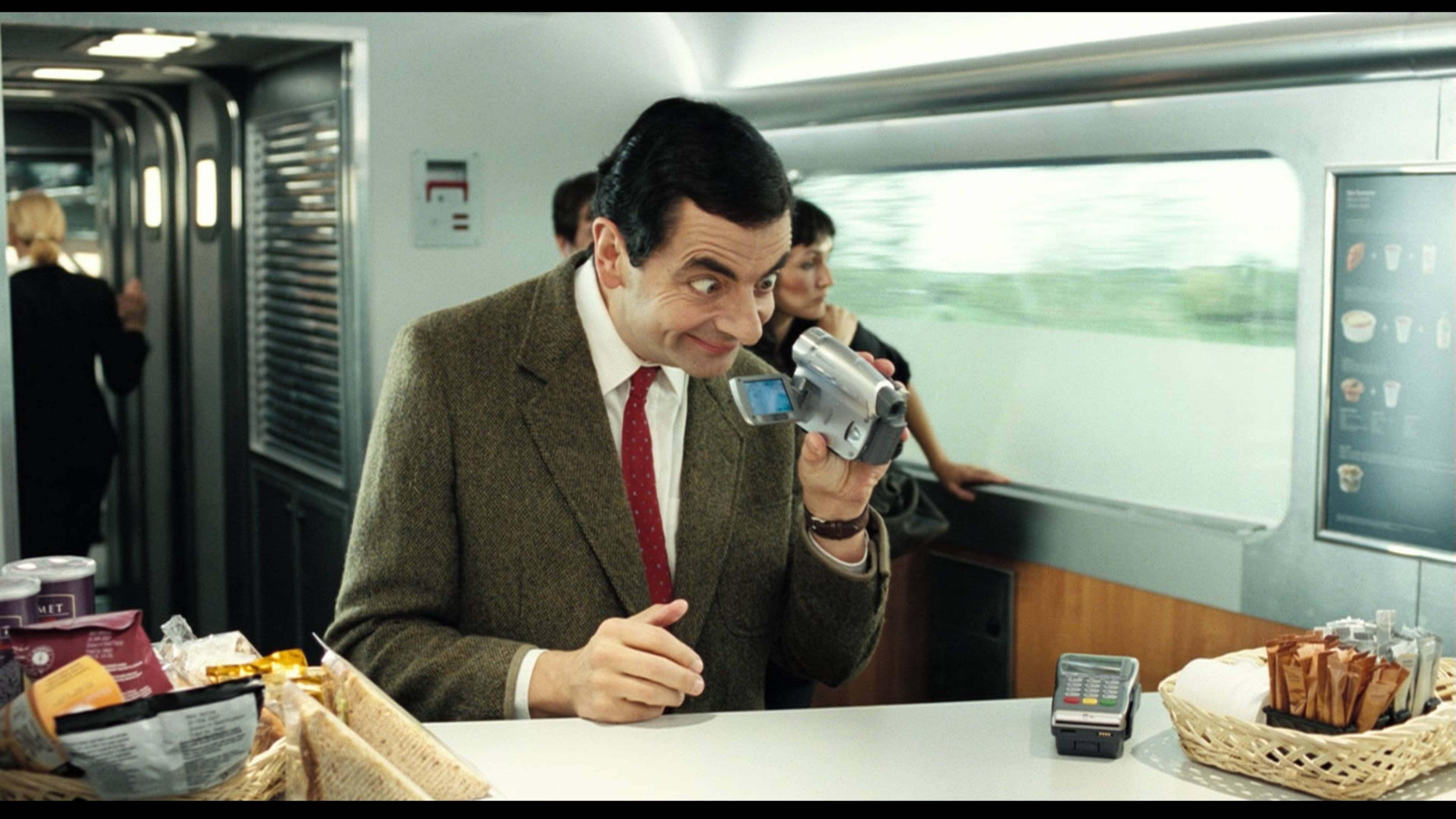 豆豆先生 桌布 壁紙 — Mr Bean 在行駛中的火車車廂內用輕便攝影機拍攝自己，露出頑皮的笑容。