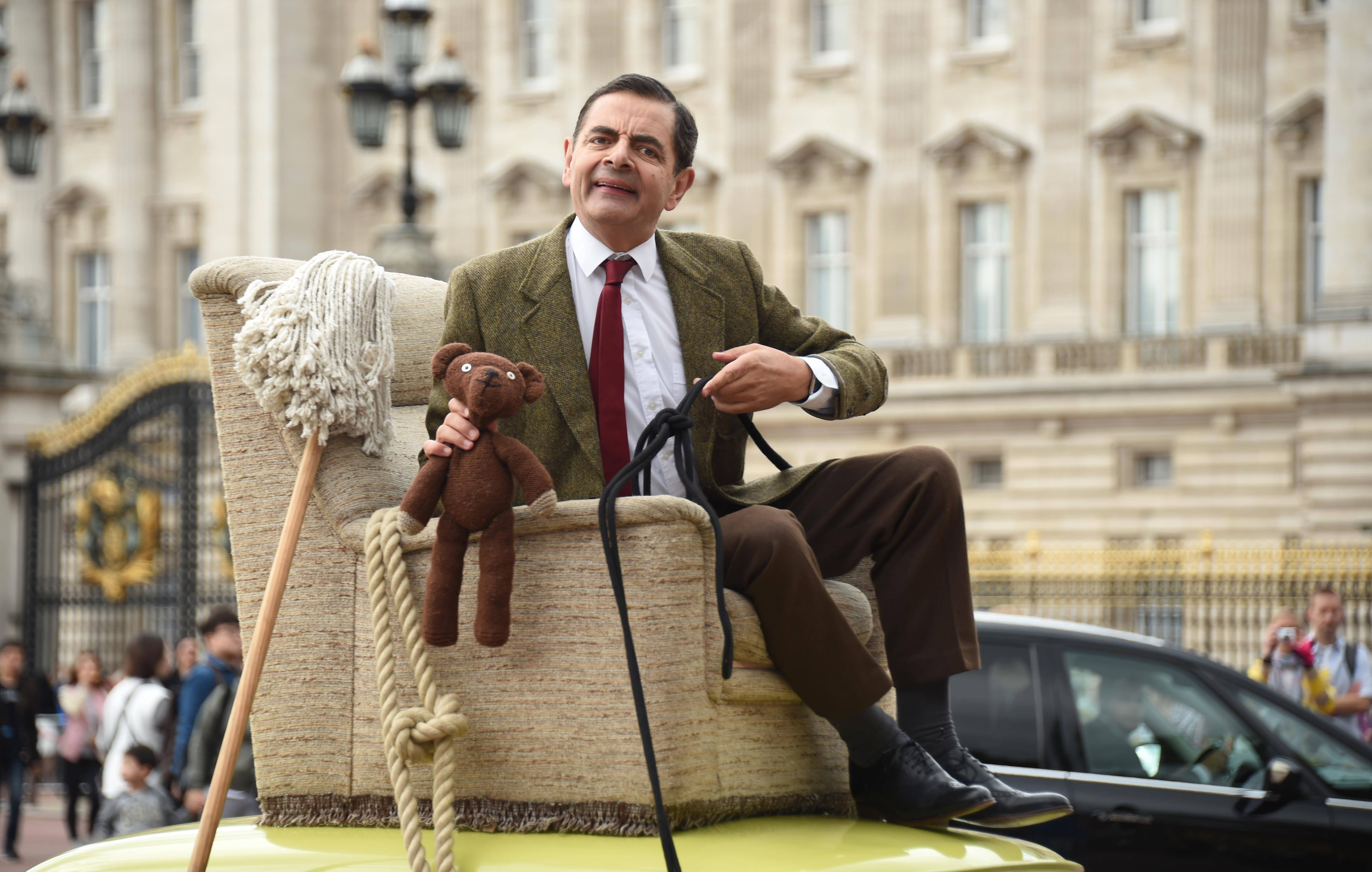 Mr Bean 坐在黃色車上，抱著泰迪熊，帶著拖把和繩子。 — 4K 壁紙