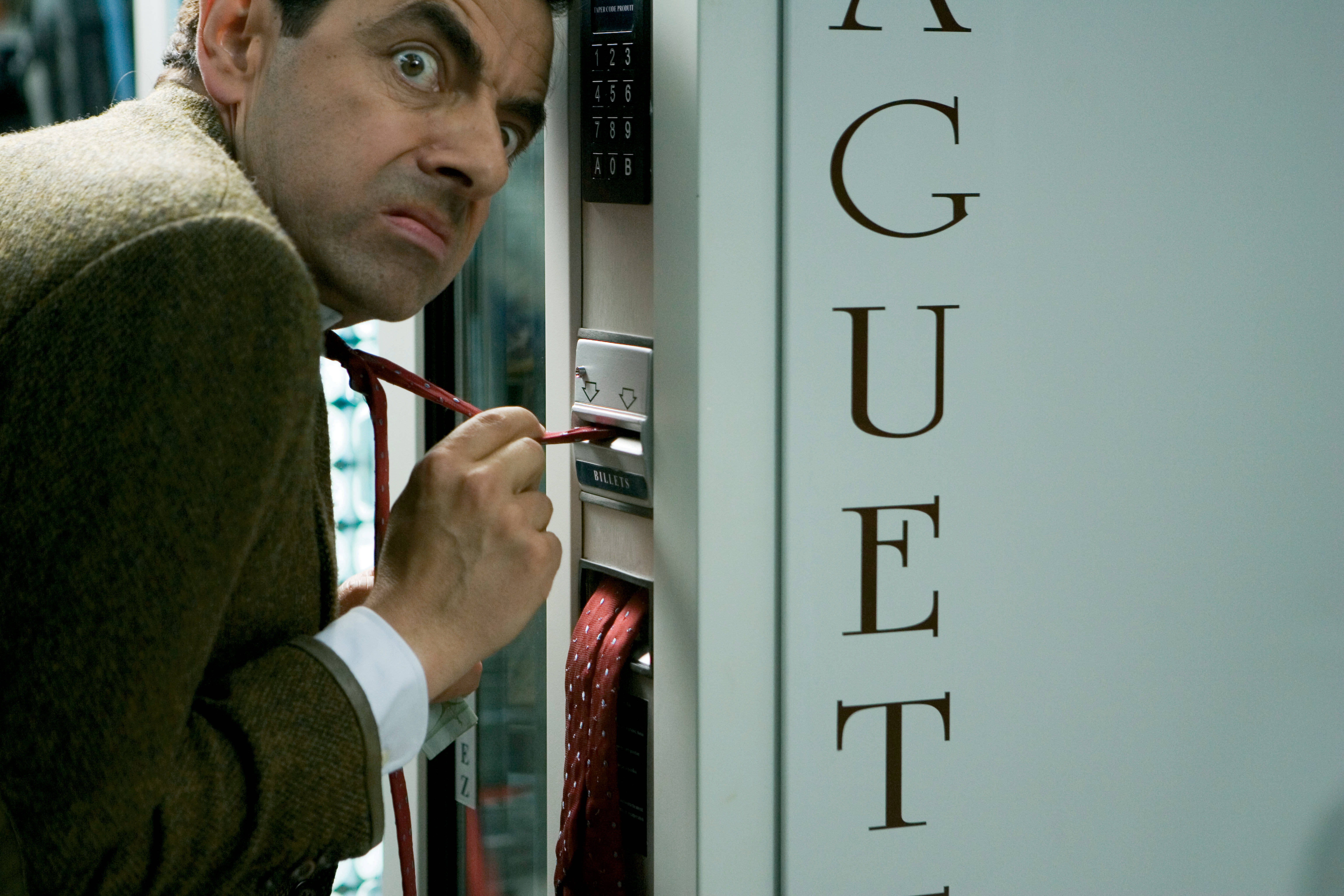4K 桌布 壁紙 — Mr Bean 專注地凝視，同時嘗試用紅色領帶作為工具操作自動販賣機。