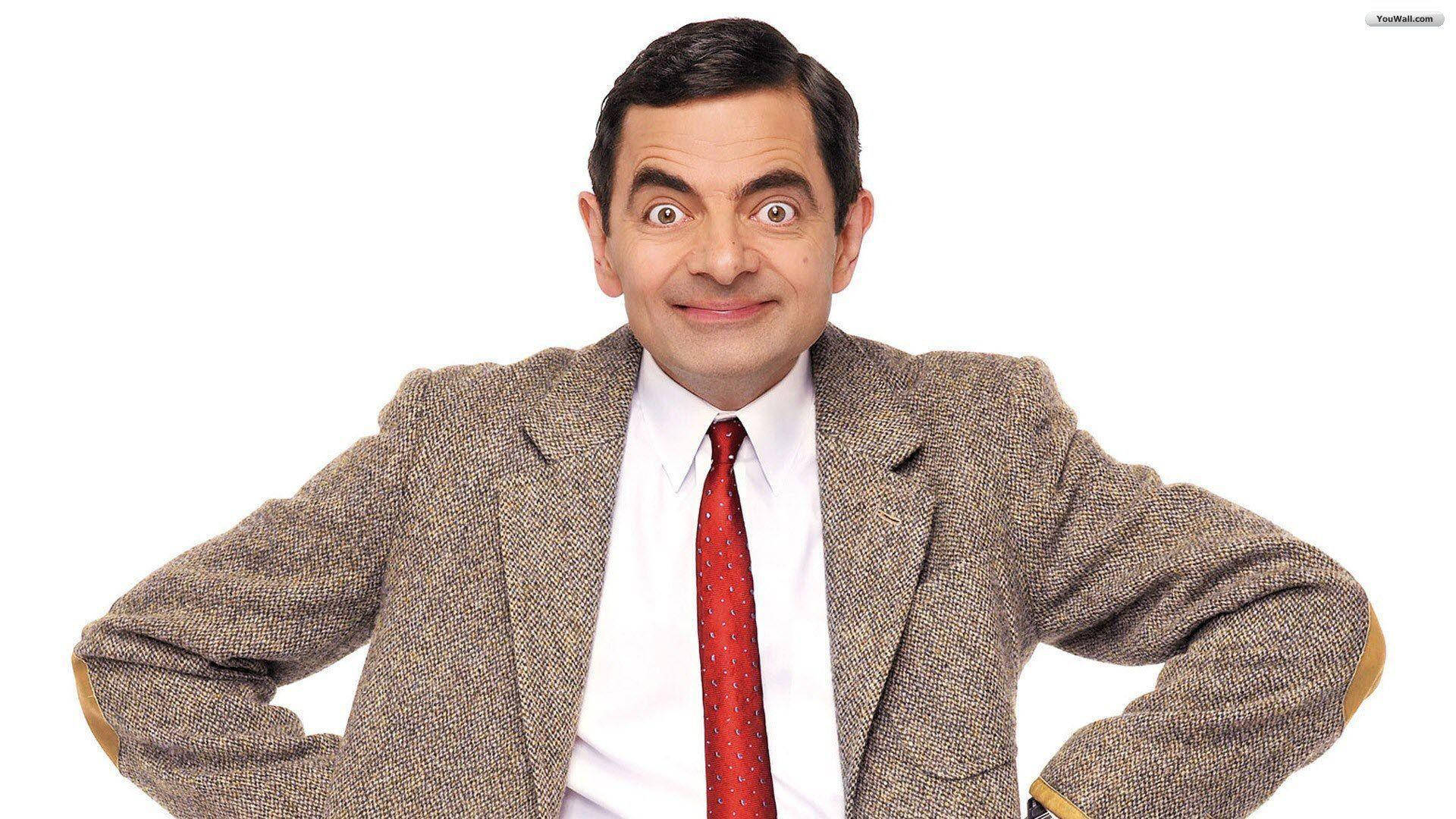 豆豆先生 桌布 壁紙 — Mr Bean 穿著粗花呢外套和紅色領帶，在純白色背景前睜大眼睛、露出狡黠笑容，擺出滑稽姿勢。