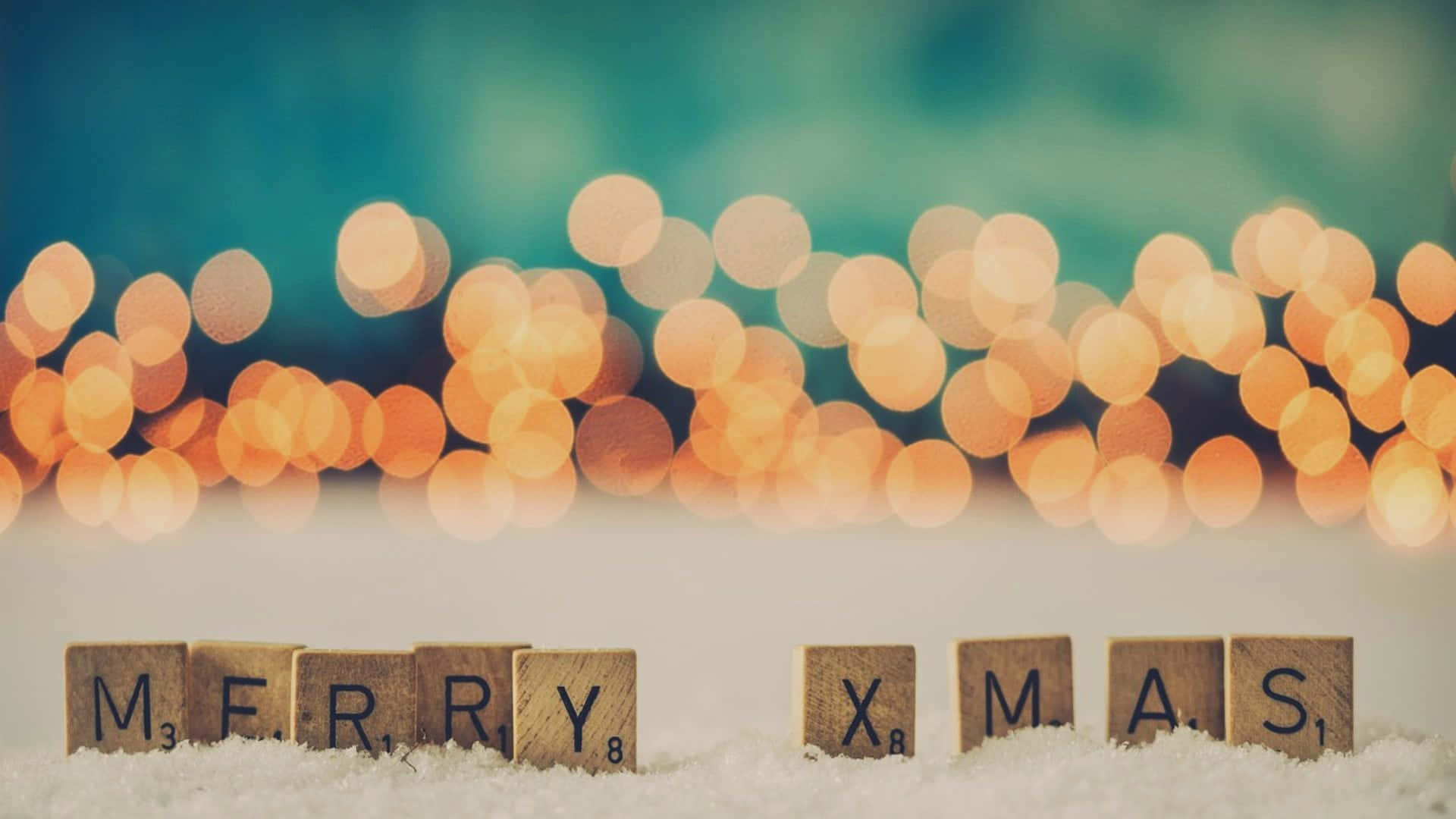  壁紙 — 木製 Scrabble 字母牌拼出 merry xmas，在雪中休息，背後有溫暖的散景燈光閃爍。