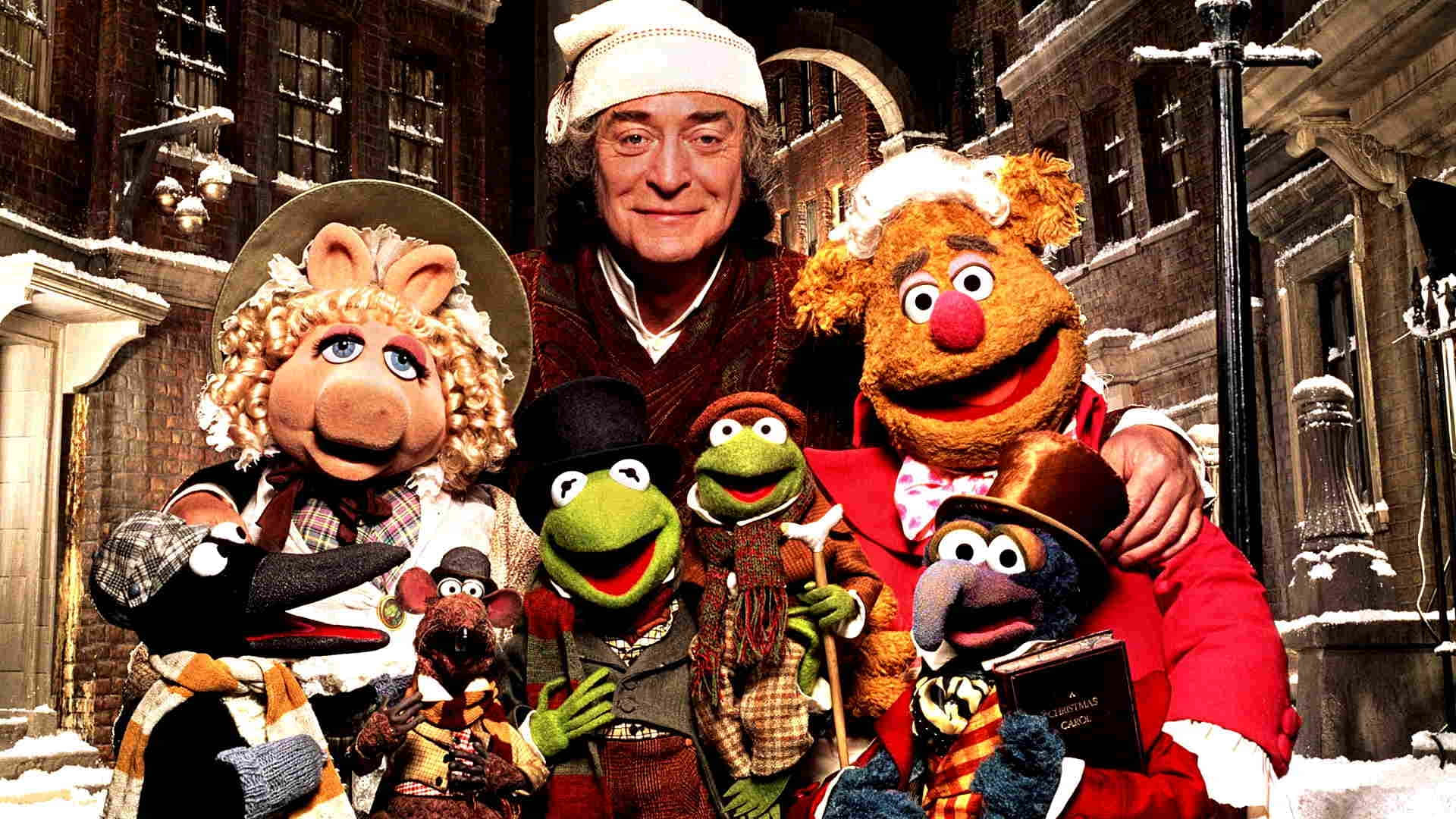  壁紙 — Muppets 和一名穿著節日冬季服裝的男子在白雪皚皚的歐洲街景中愉快地擺姿勢。