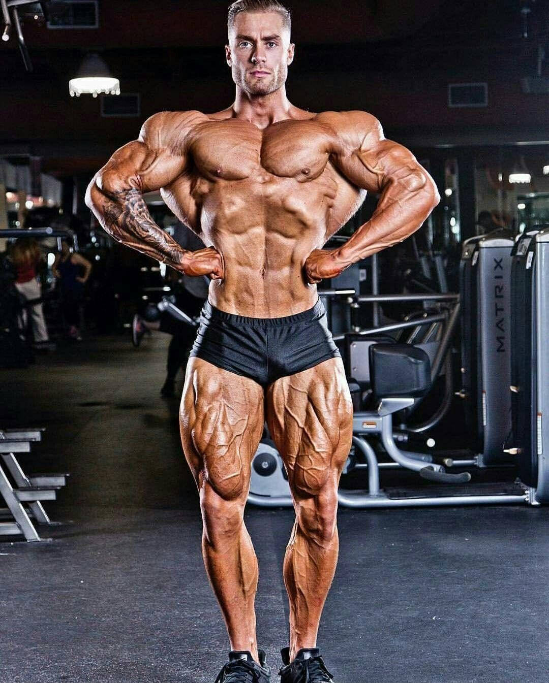 一位肌肉發達的男子在健身房展示清晰的肌肉和刺青。 — Chris Bumstead 壁紙