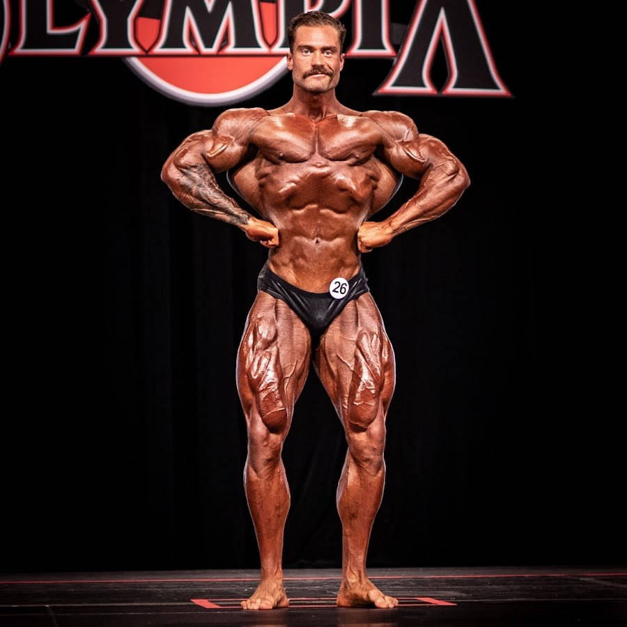 一位健美運動員在奧林匹亞比賽的舞台上擺姿勢。 — Chris Bumstead 壁紙