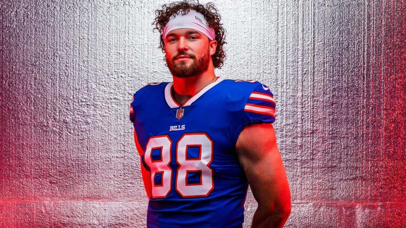  壁紙 — 一位肌肉發達的足球員身穿藍色 Bills 球衣（88號），自信地站在充滿紅色和銀色光線的紋理金屬牆前。