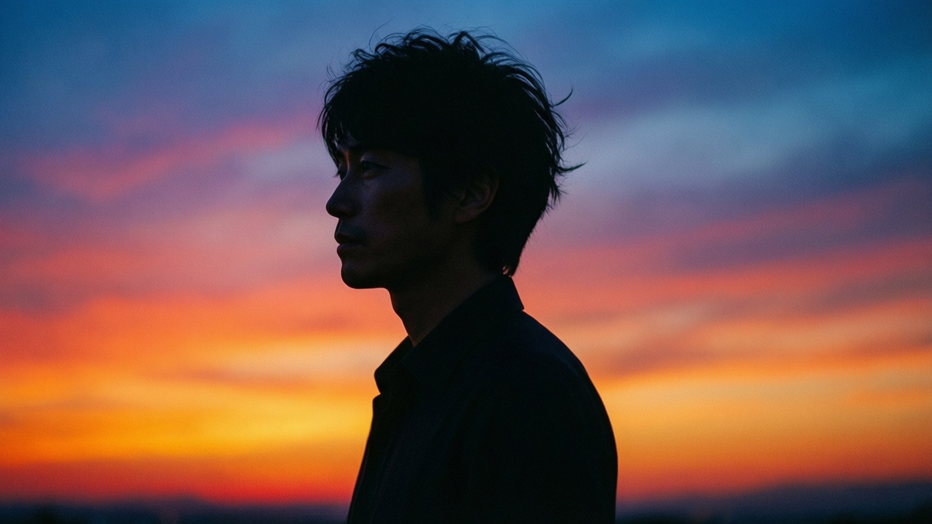 Silhouette Sunset 壁紙 — 一個男人的剪影若有所思地凝視著充滿活力的日落天空，天空中有橙色、粉紅色和深藍色的雲彩條紋。