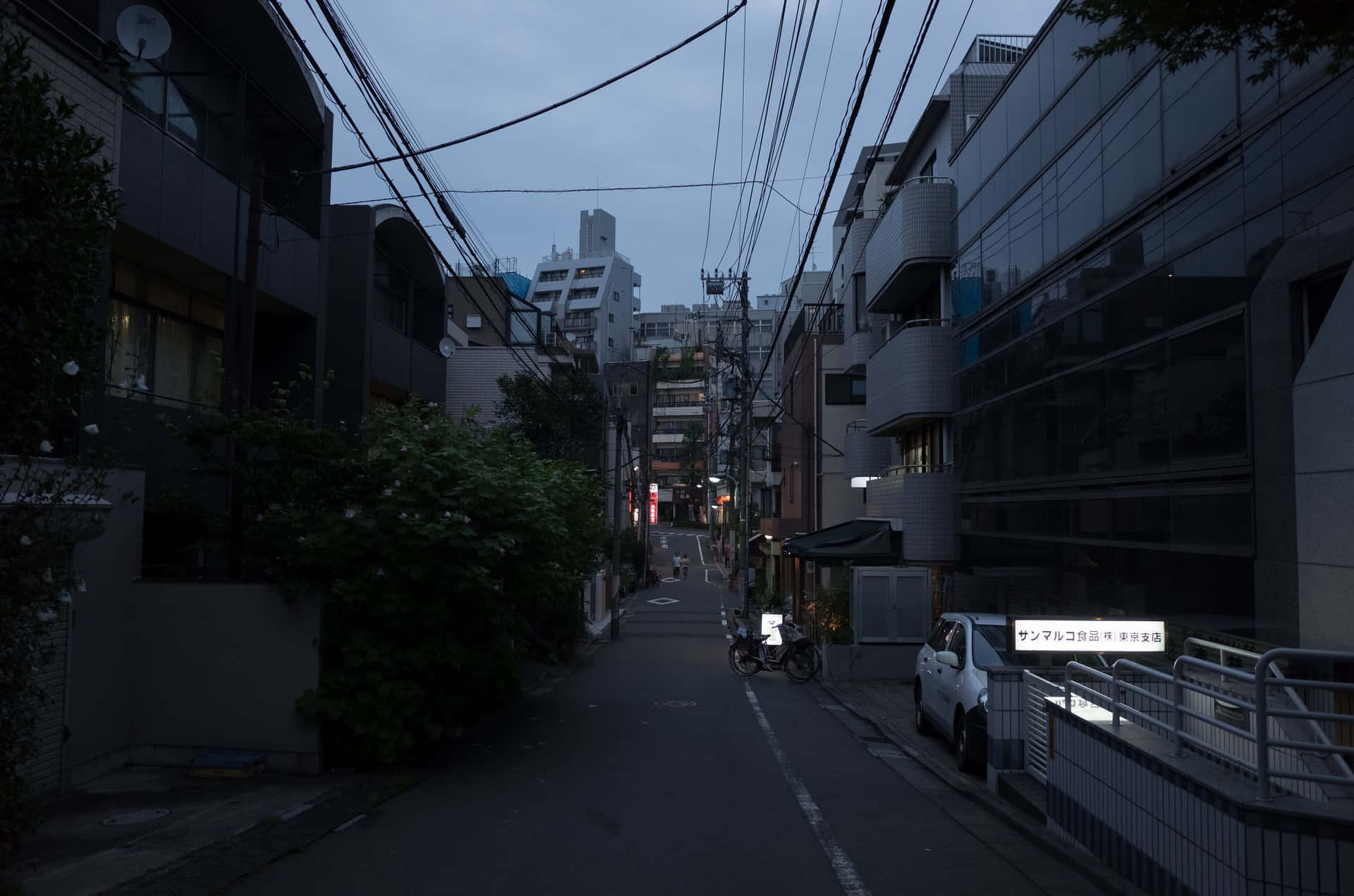 黃昏時分燈光昏暗的城市小巷，停放的汽車和現代建築。 — 日式暗黑 壁紙