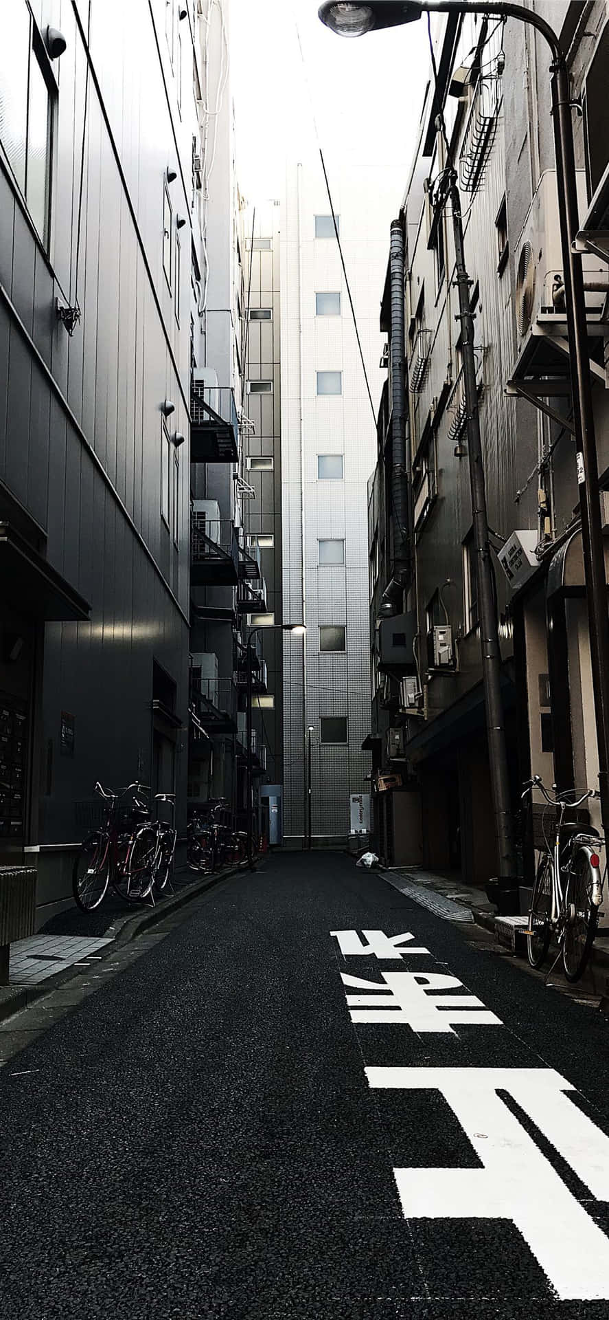 路燈下停有自行車和日本道路標記的狹窄城市小巷。 — 日式暗黑 壁紙